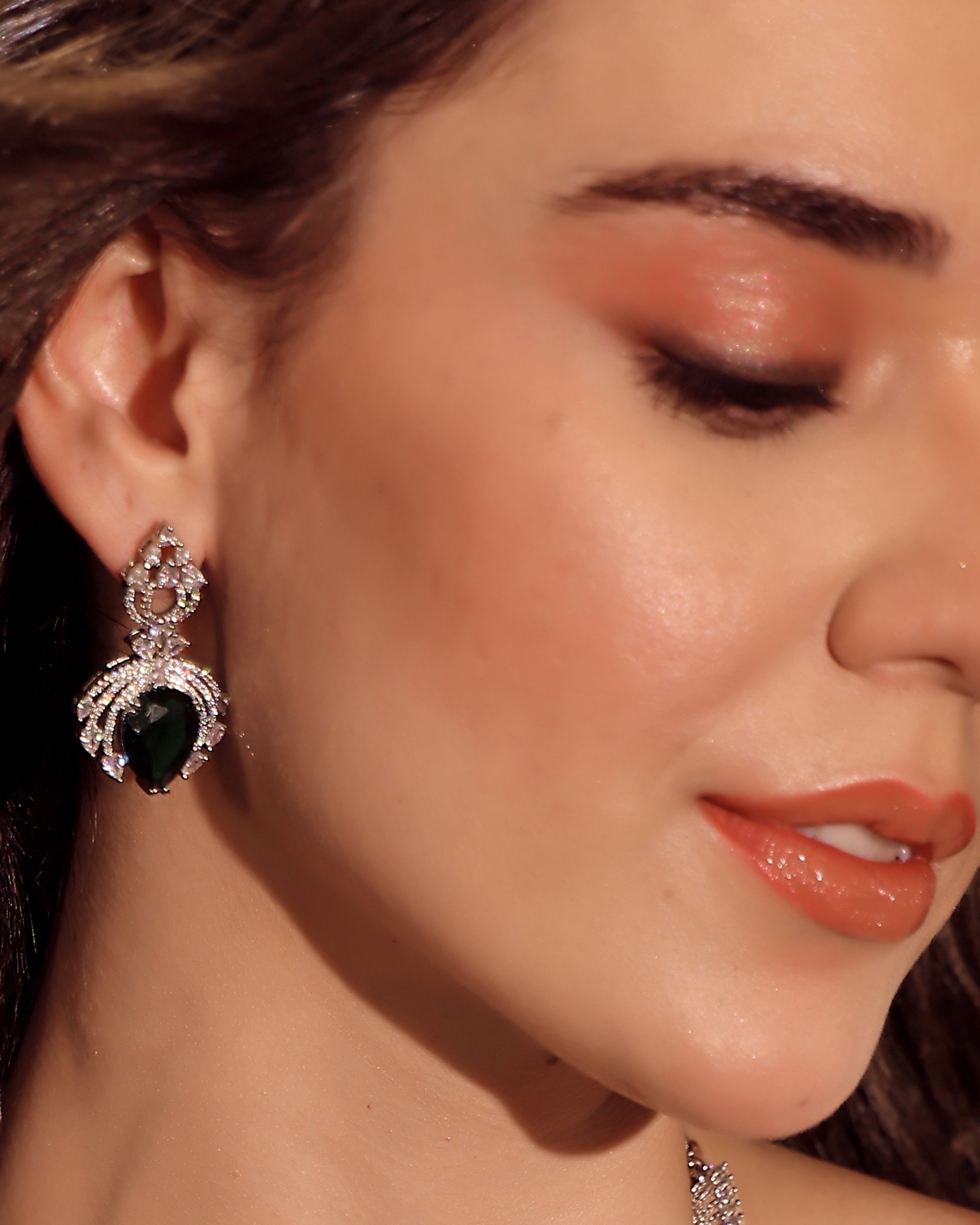 Close-up of a woman wearing a green teardrop earring with a diamond-like stone.