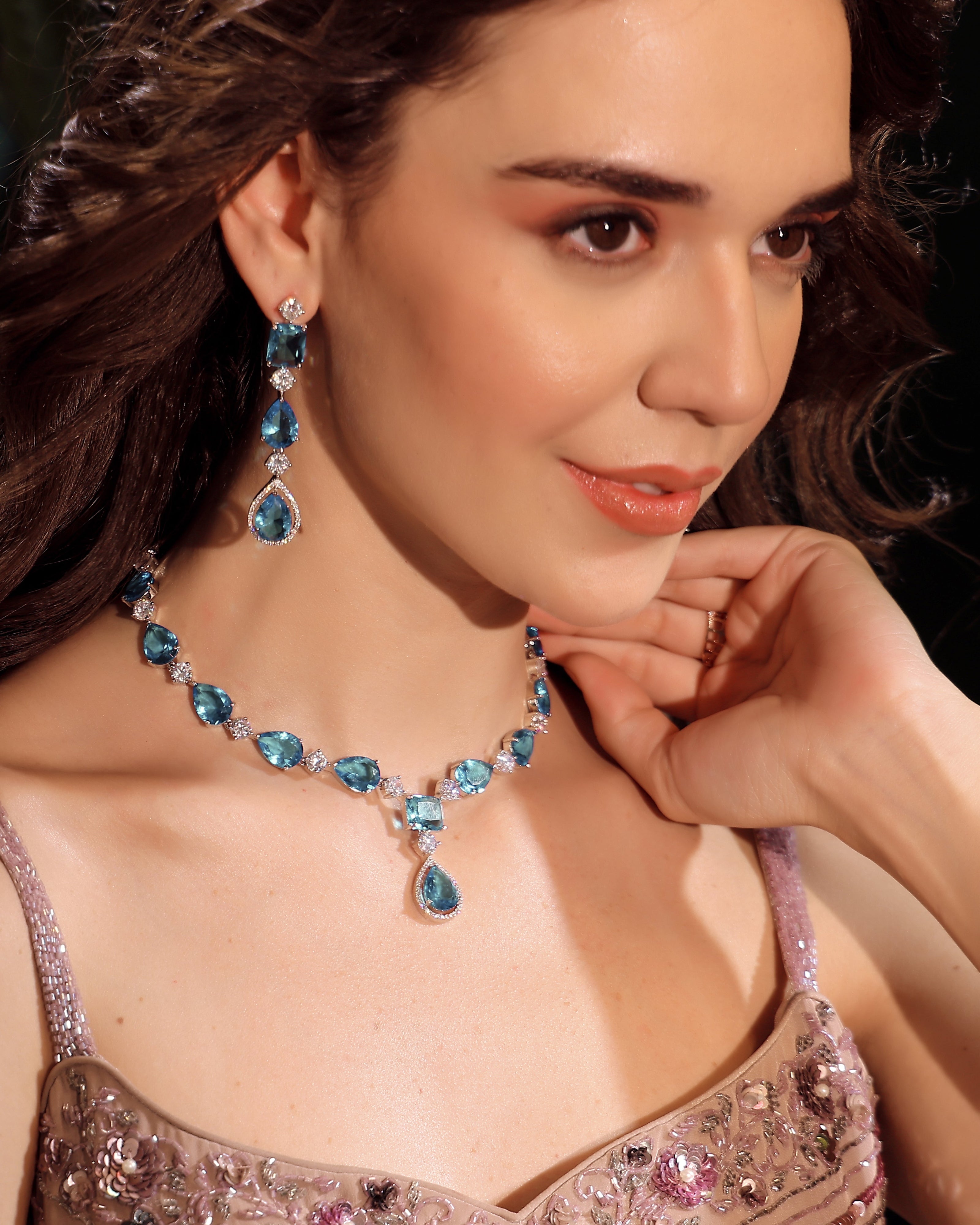 Woman wearing a blue gemstone necklace and earrings with a dark background