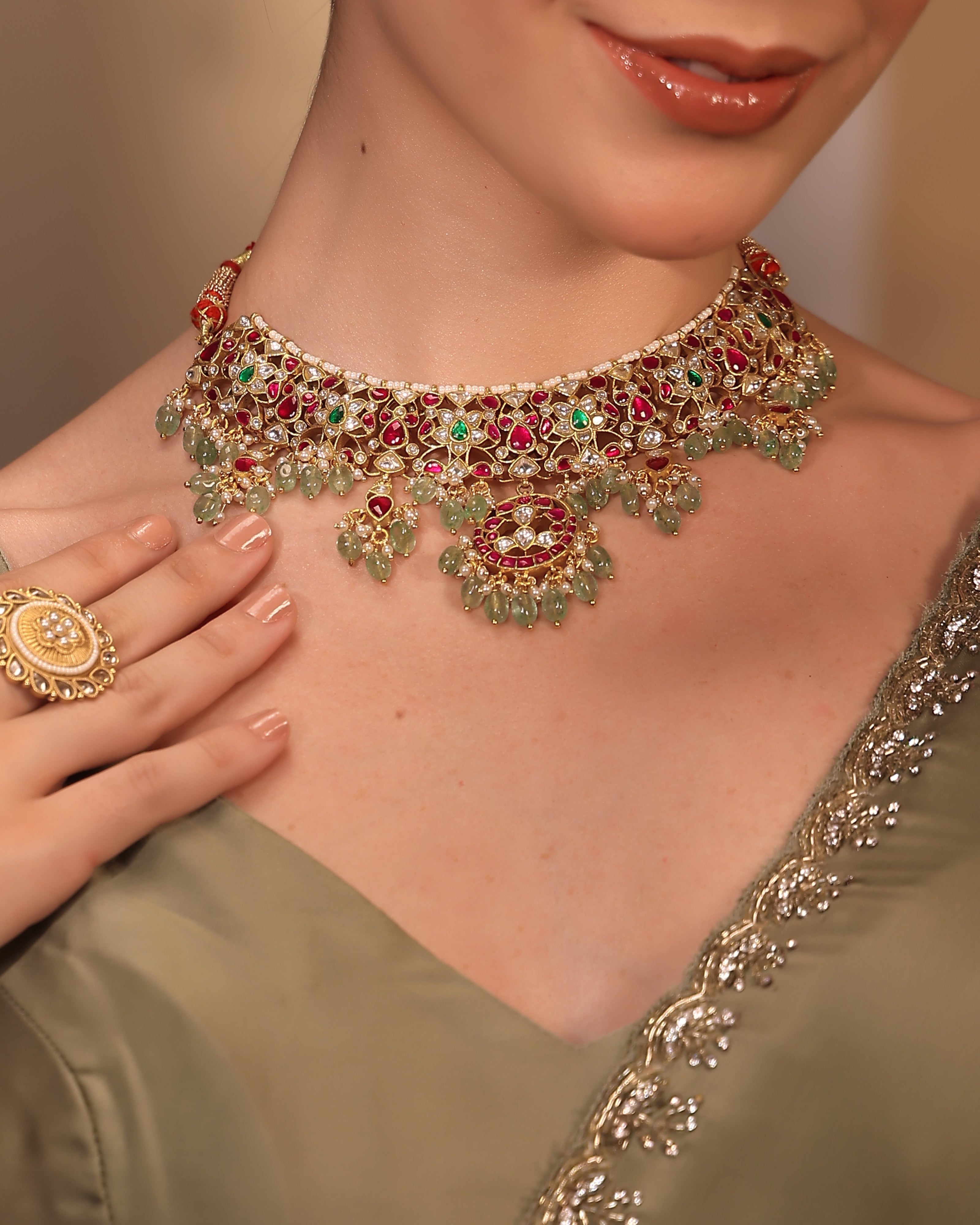 Close-up of a woman wearing an ornate necklace with gemstones, set against a neutral background.