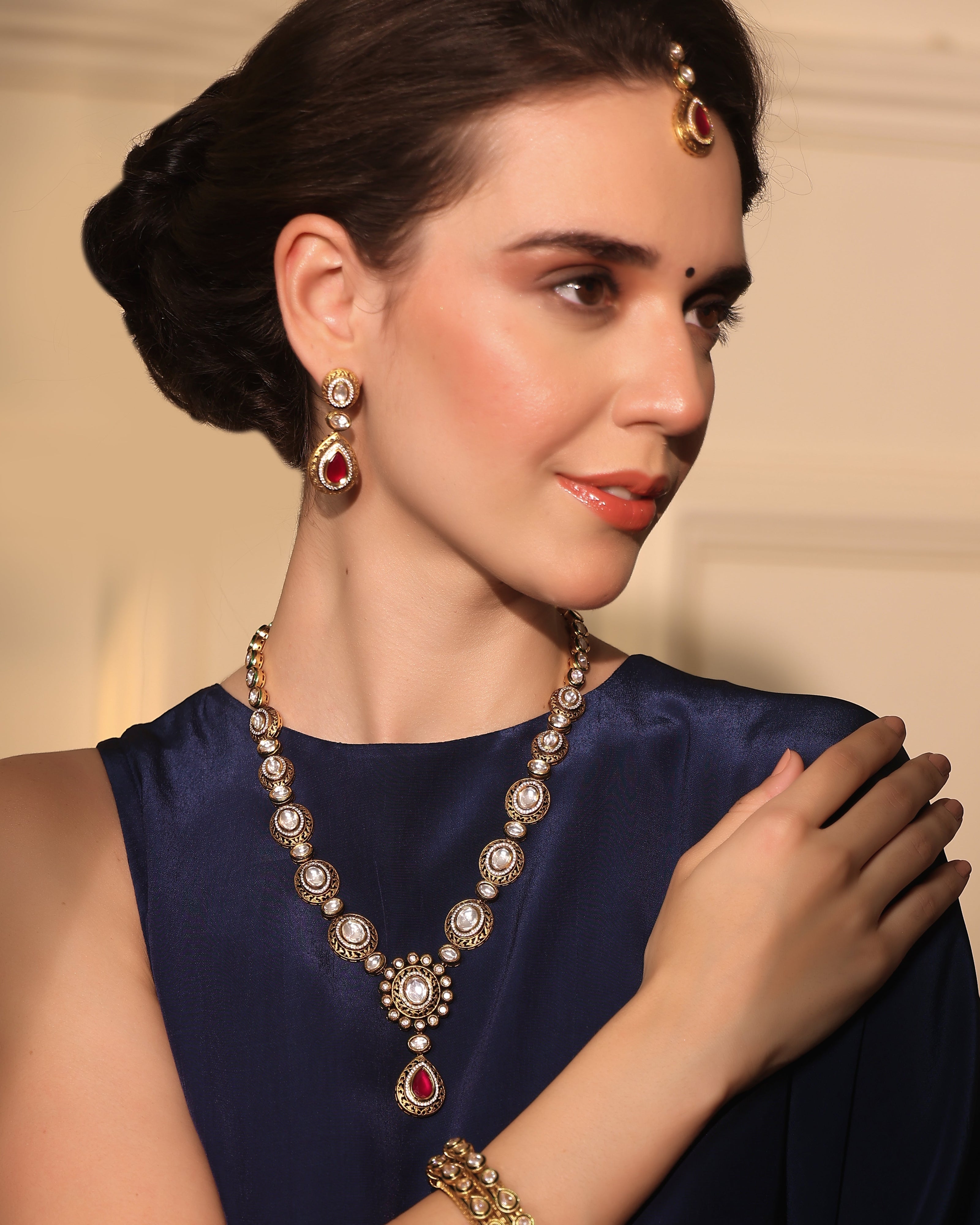 Woman wearing a necklace, earrings, and bracelet with a neutral background