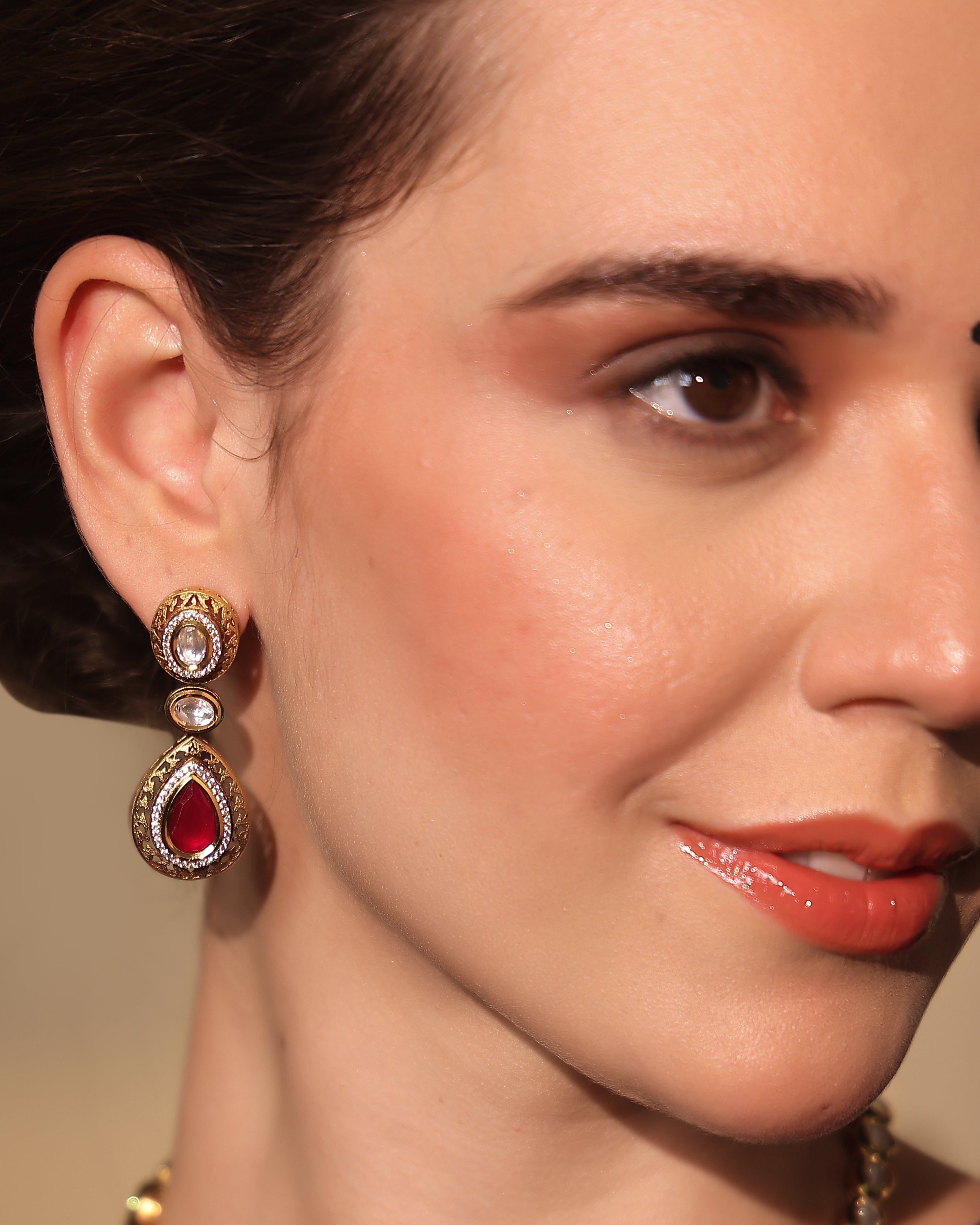 Close-up of a woman wearing gold earrings with red gemstones.