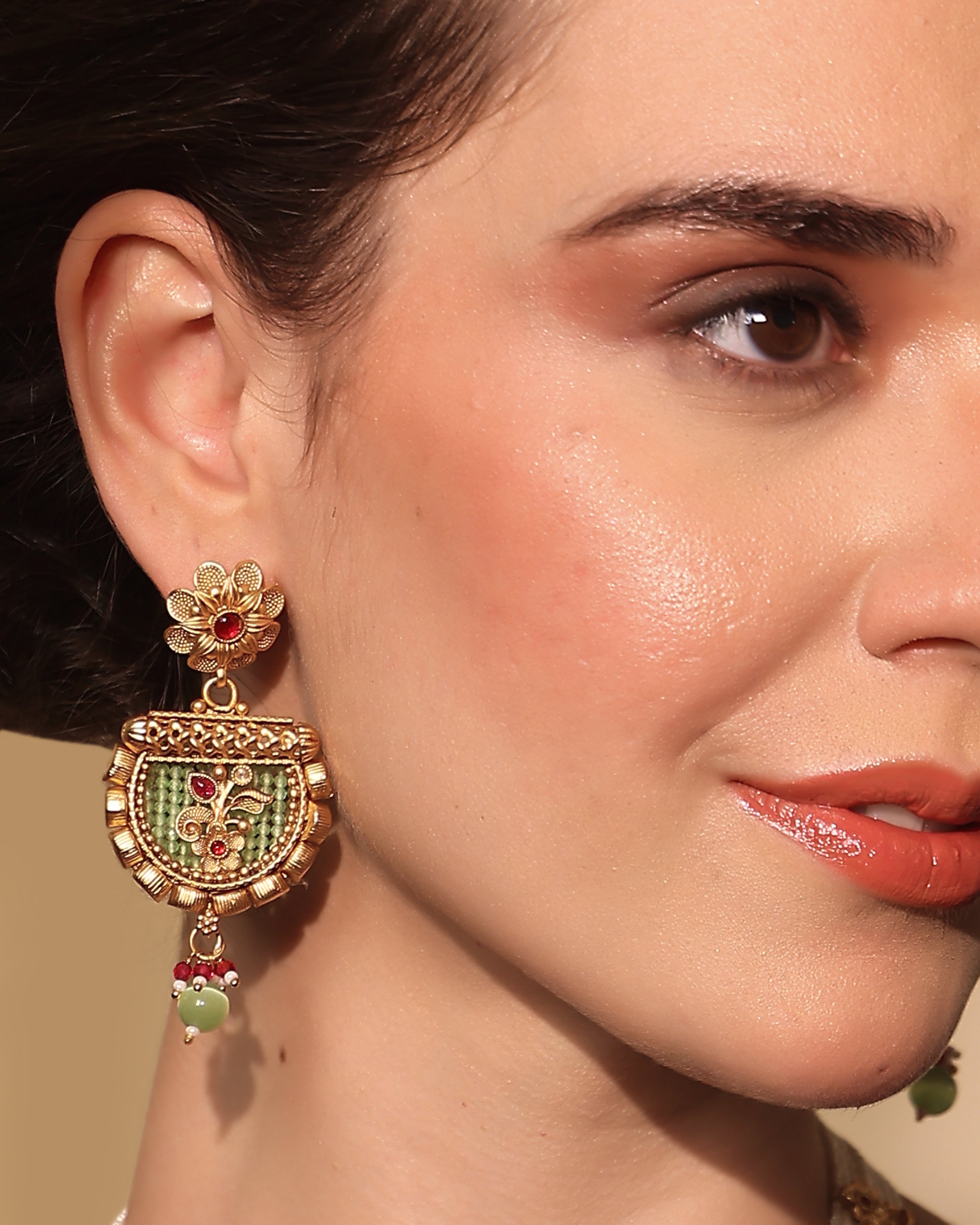 Close-up of a woman wearing an ornate earring with intricate design and colorful gemstones.
