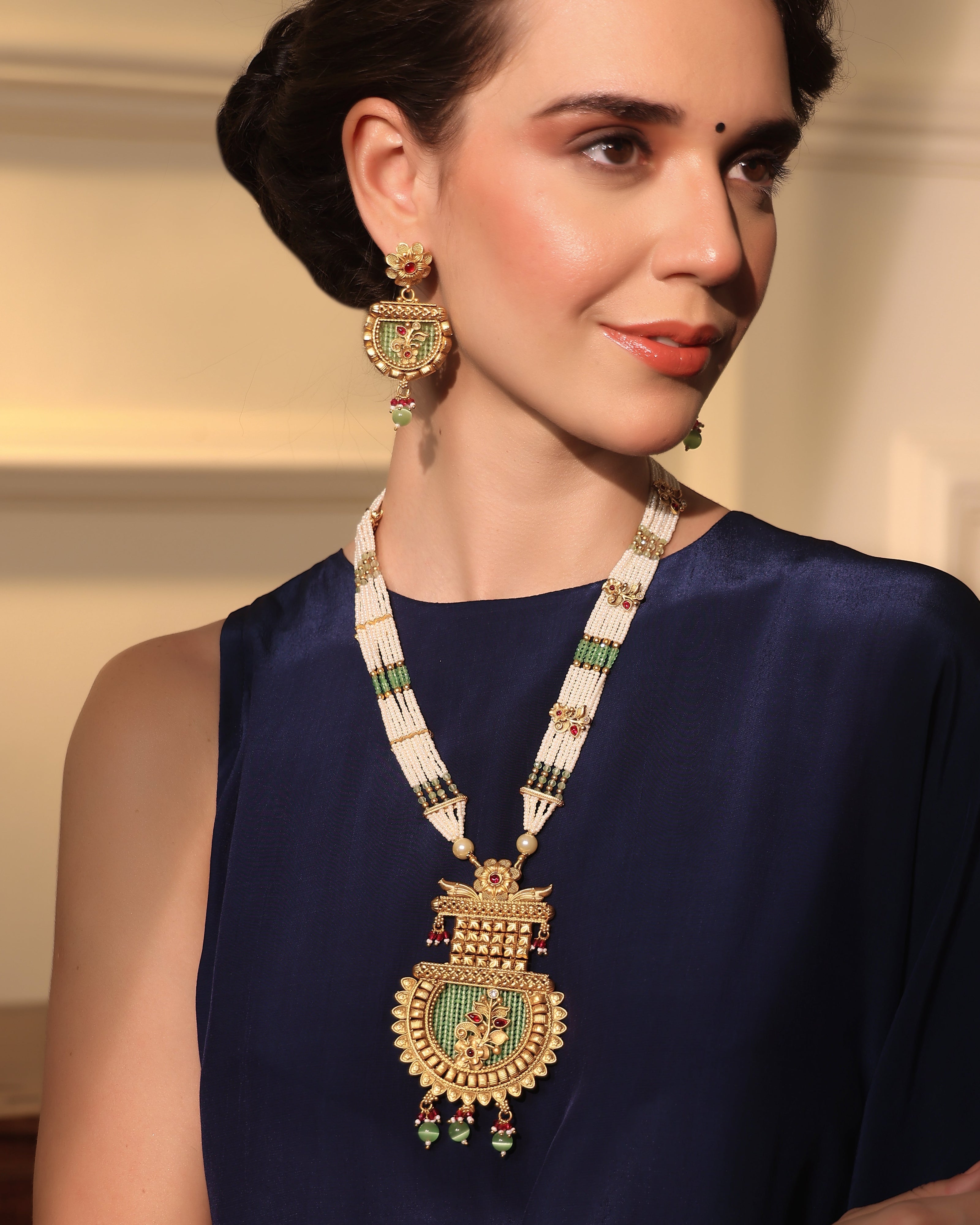 Woman wearing a traditional gold necklace and earrings against a neutral background