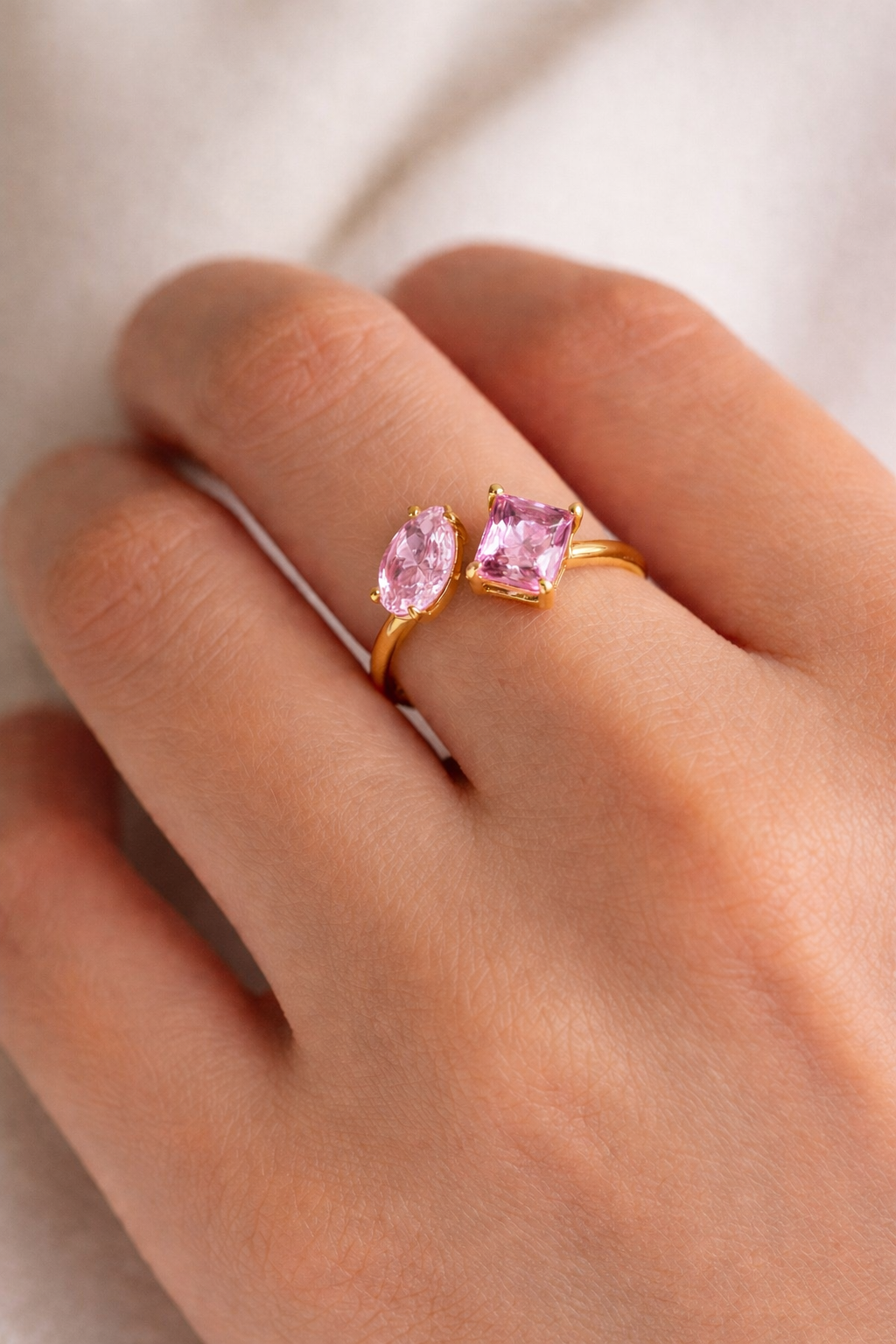 Gold ring with pink gemstones on a hand against a neutral background