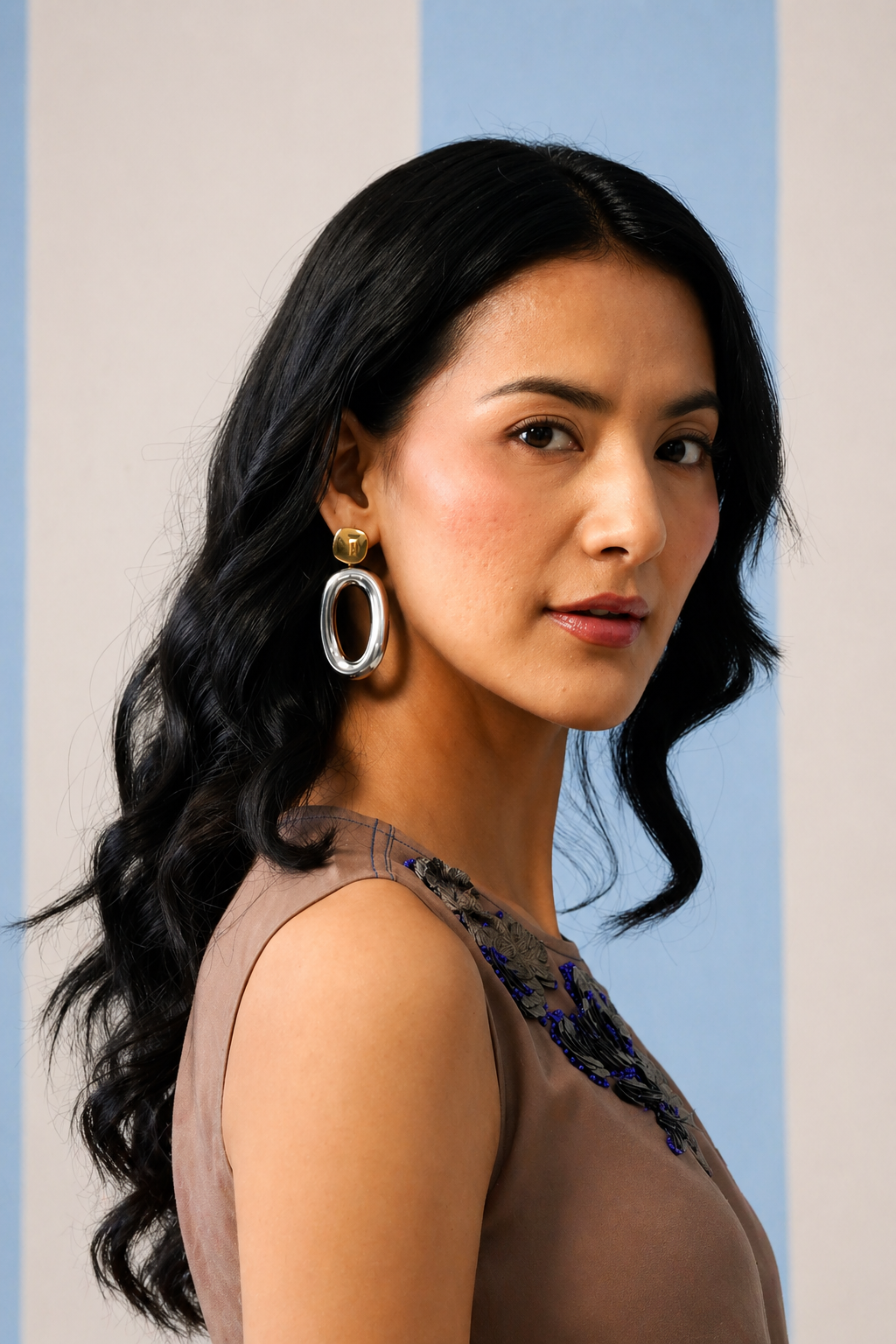 Woman with long dark hair wearing hoop earrings against a light blue and beige background