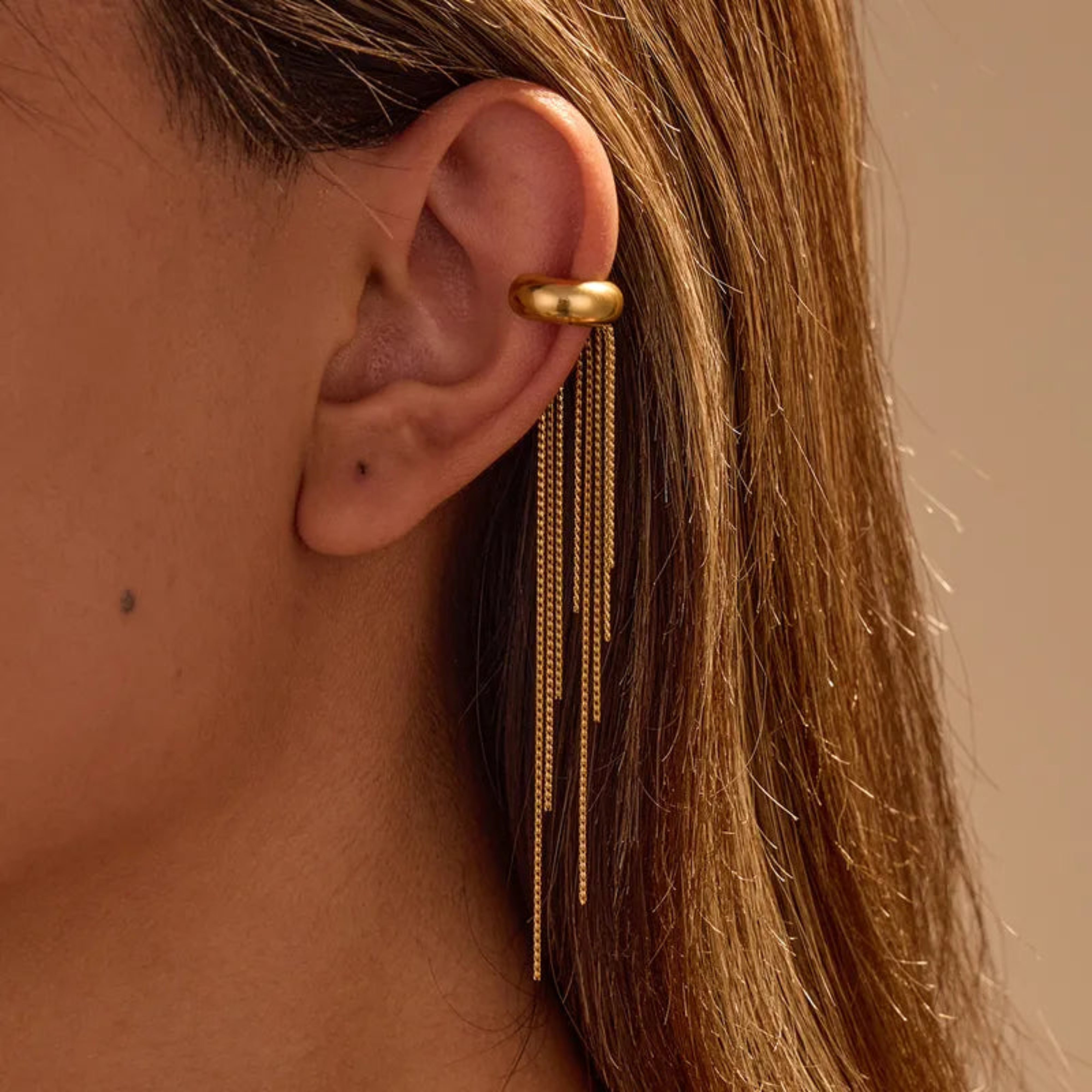 Close-up of a person wearing a gold earring with dangling chains.