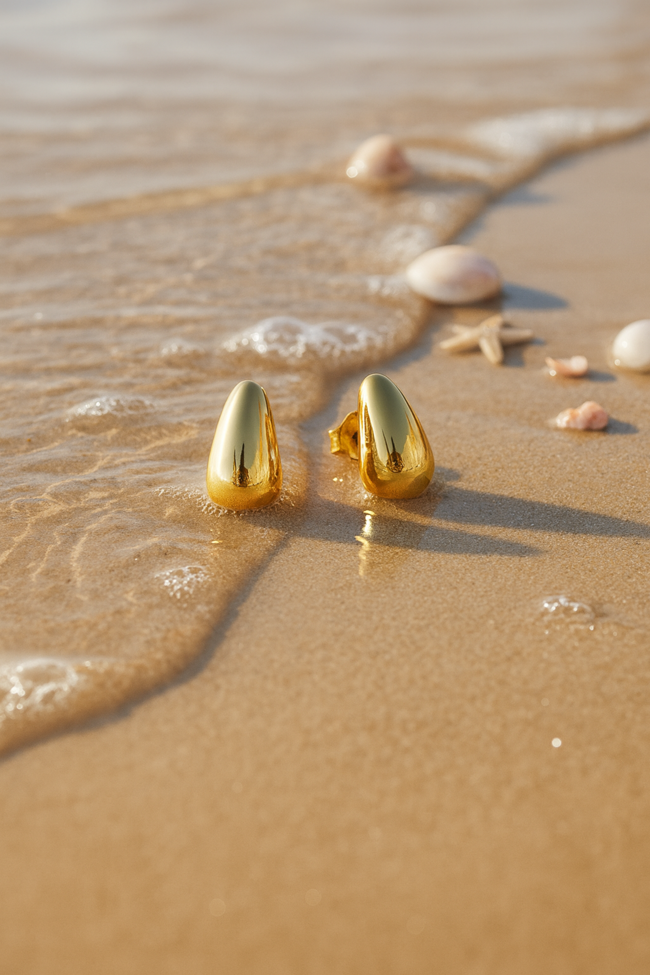 Gold earrings on a sandy beach with small shells and starfish.