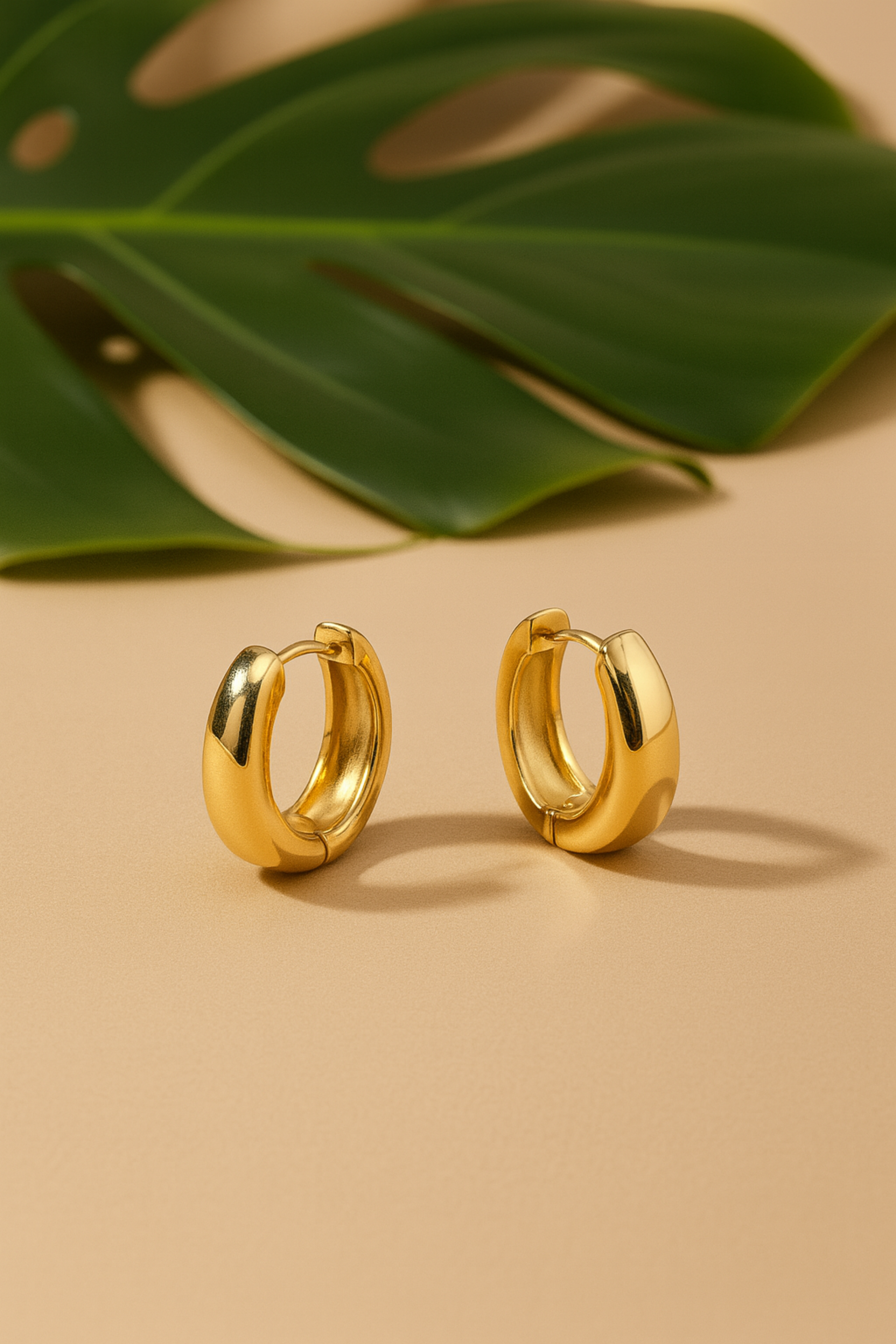 Gold hoop earrings on a beige background with a green leaf