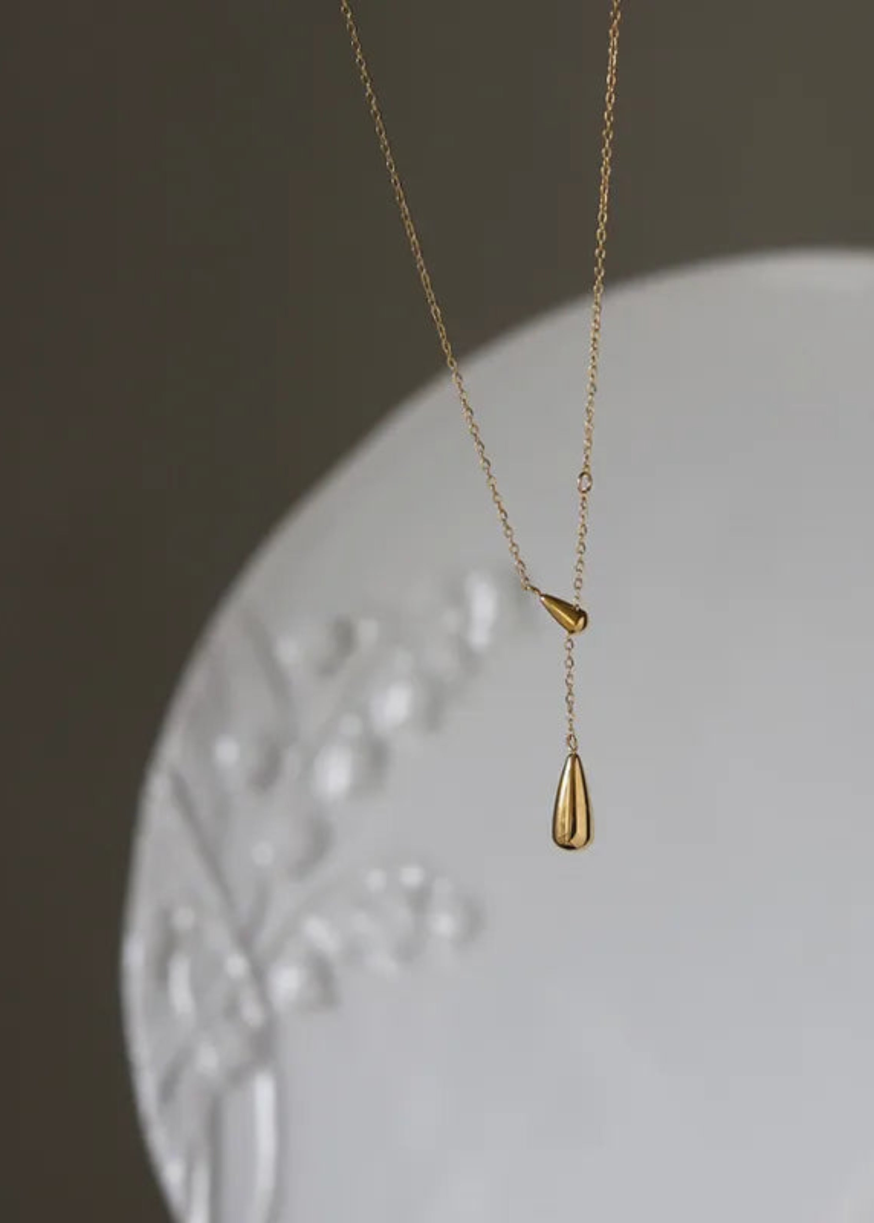 Gold necklace with a teardrop pendant on a white surface with a dark background