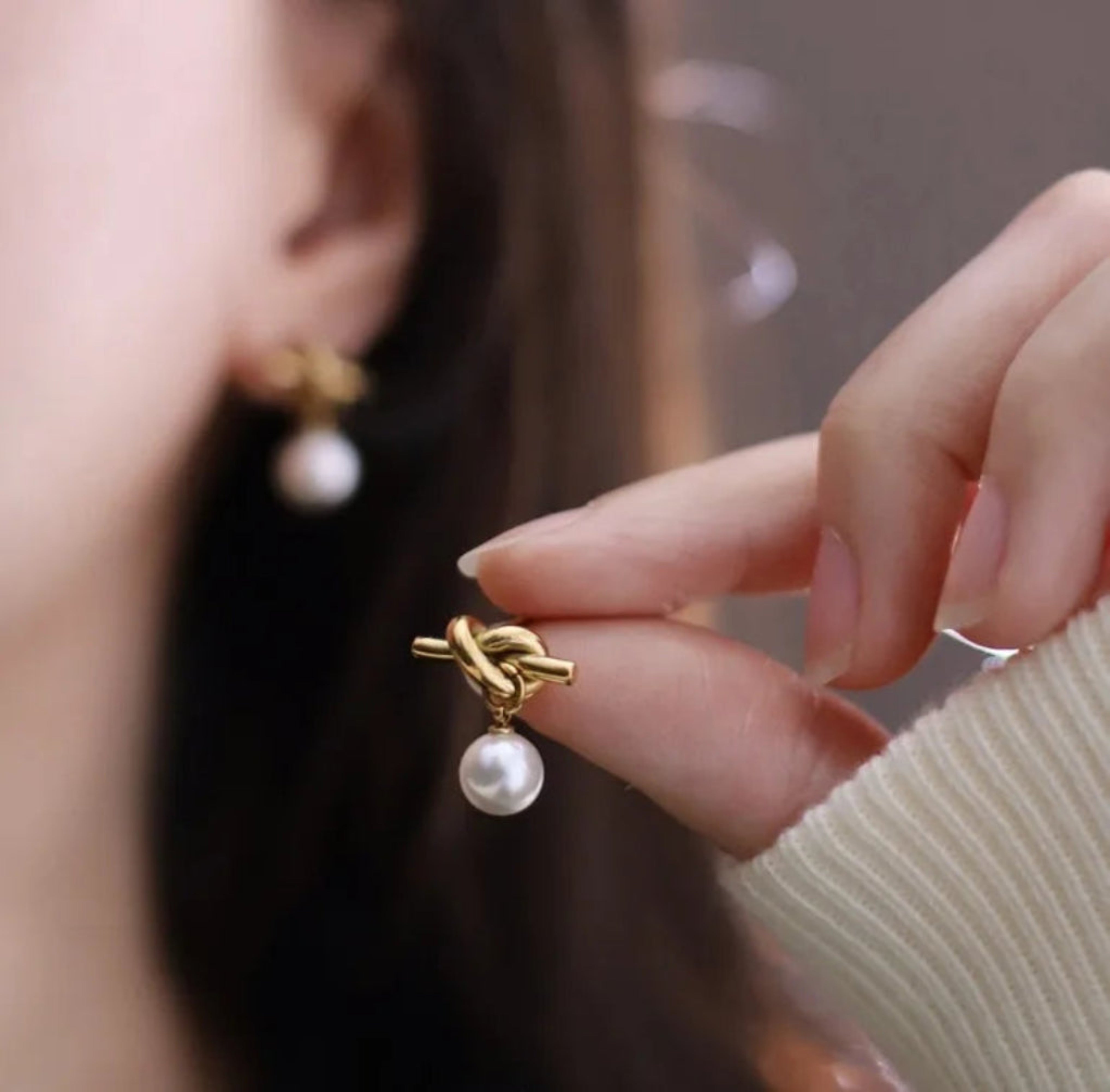 Close-up of a hand holding a gold earring with a pearl detail.
