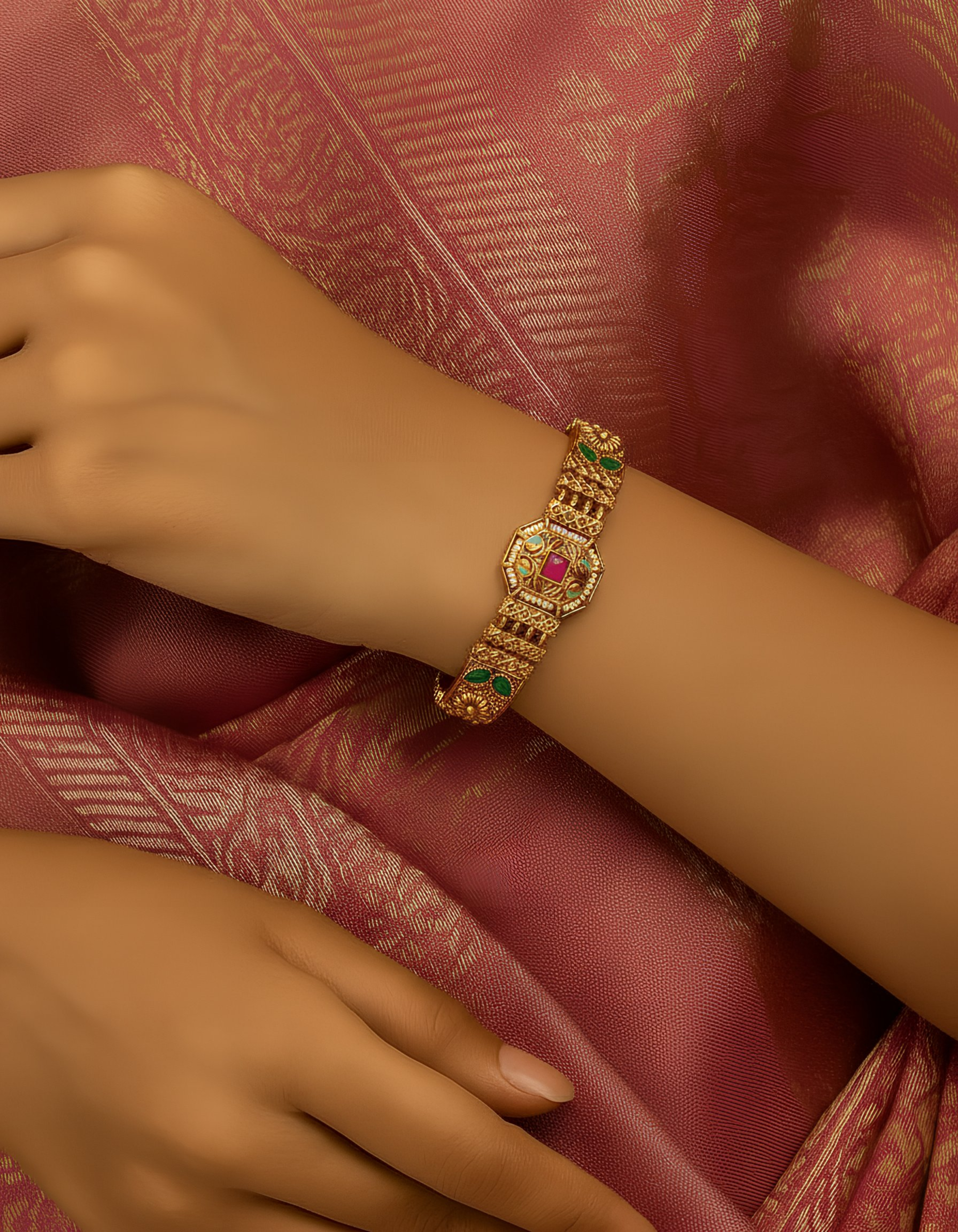 Gold bracelet with gemstones on a wrist against a pink fabric background