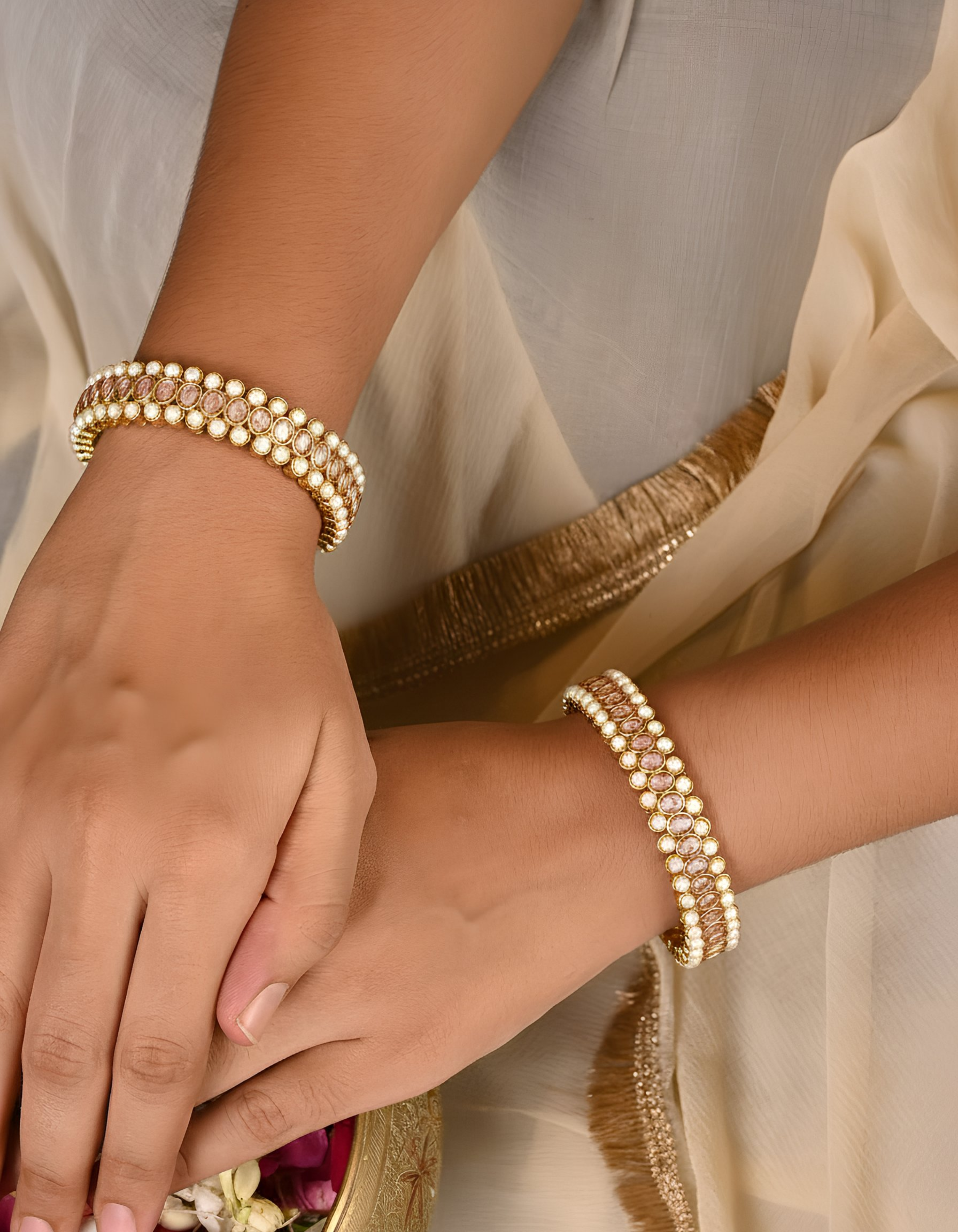 Close-up of hands wearing gold bracelets with a neutral background