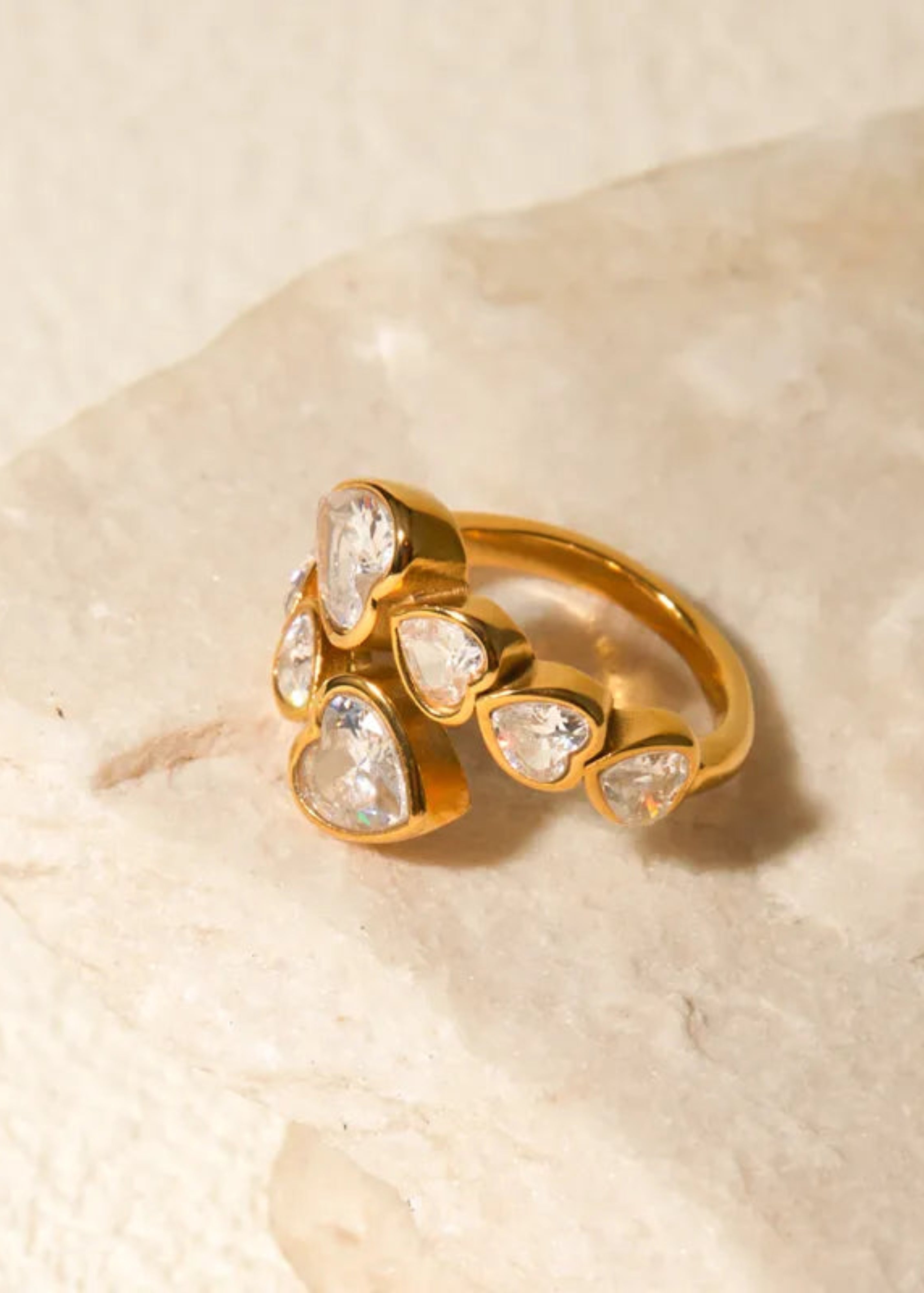 Gold ring with teardrop-shaped gemstones on a beige stone background