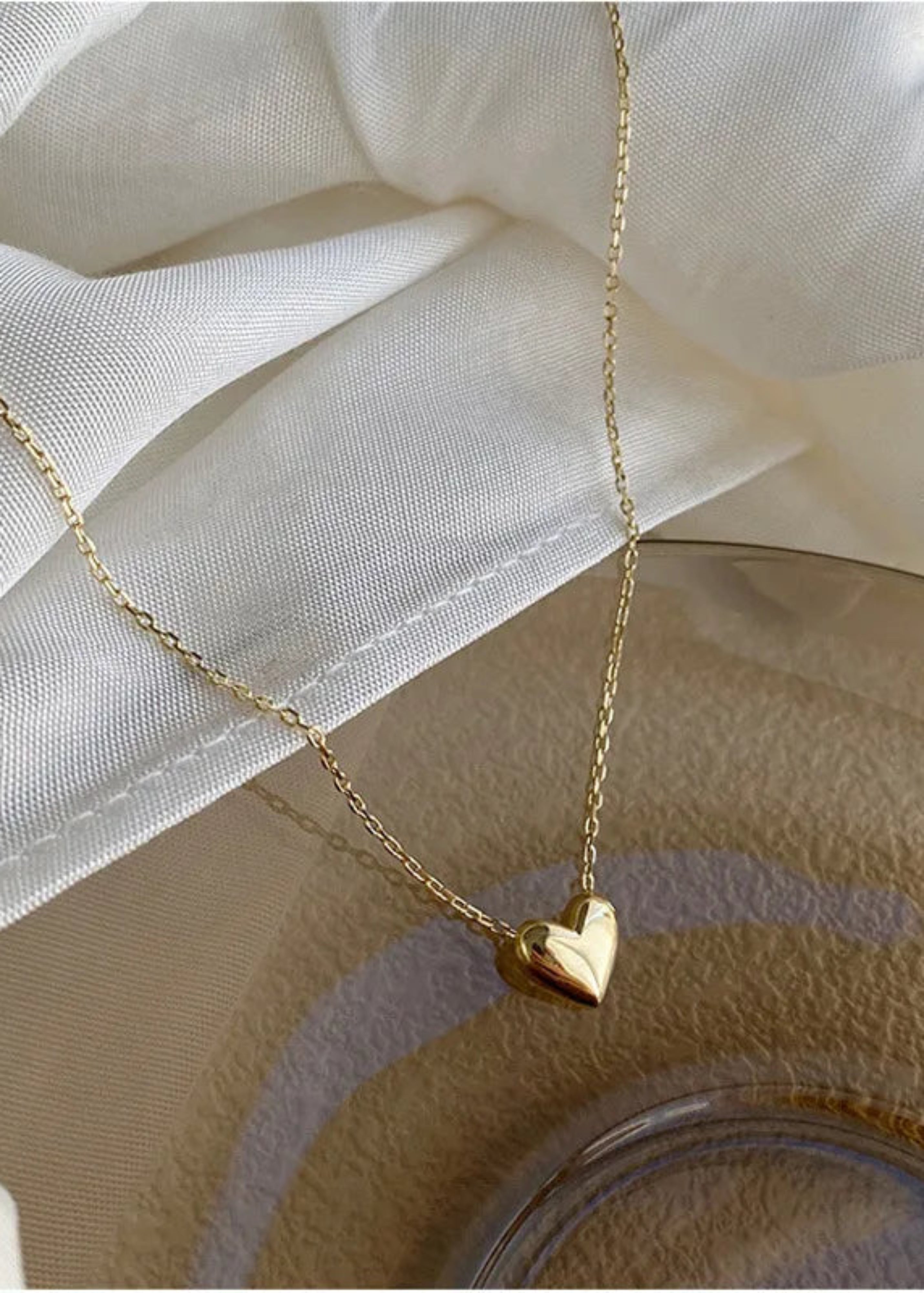 Gold heart-shaped pendant necklace on a white fabric background