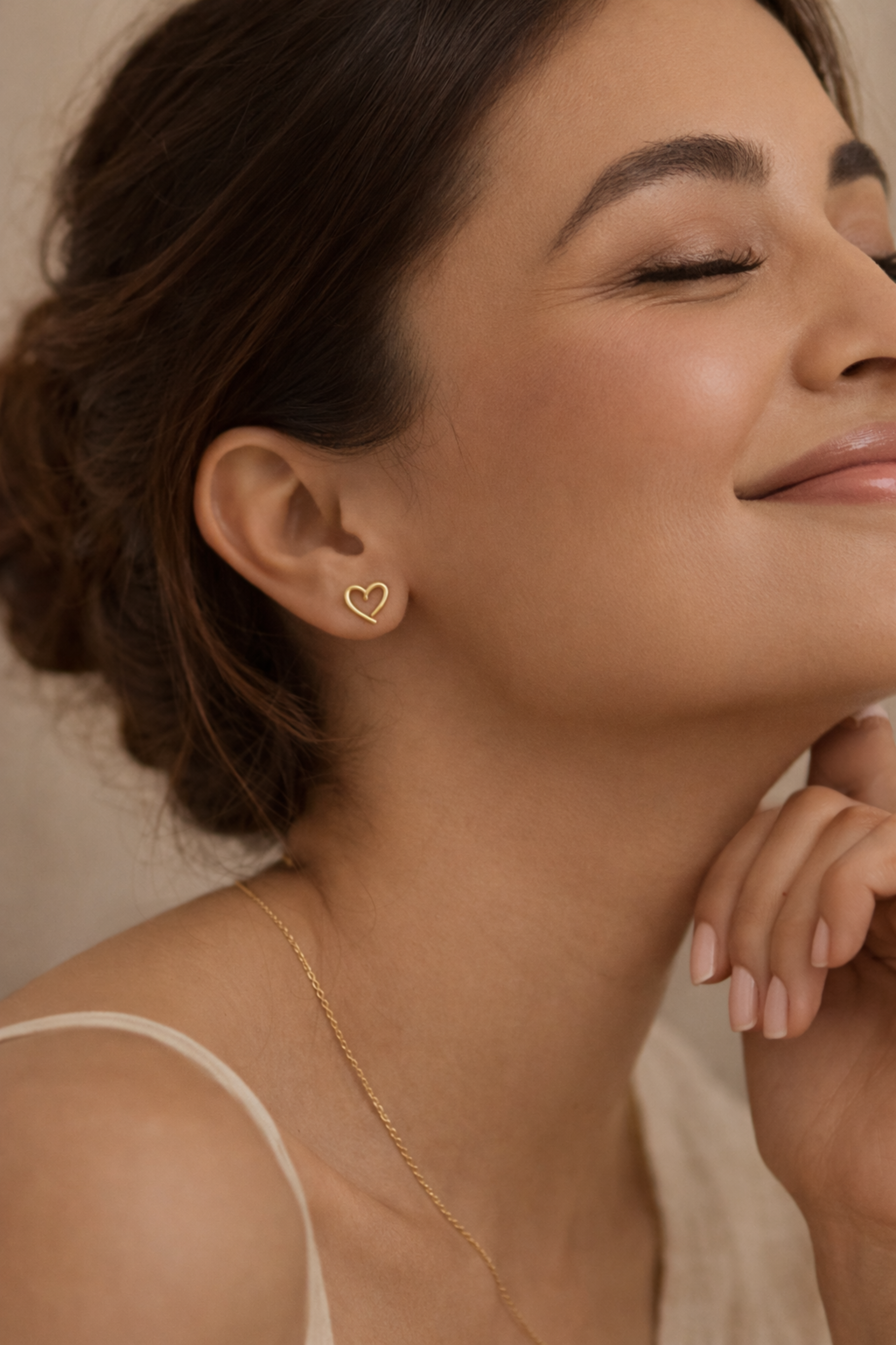 Close-up of a woman wearing a gold heart-shaped earring with a neutral background