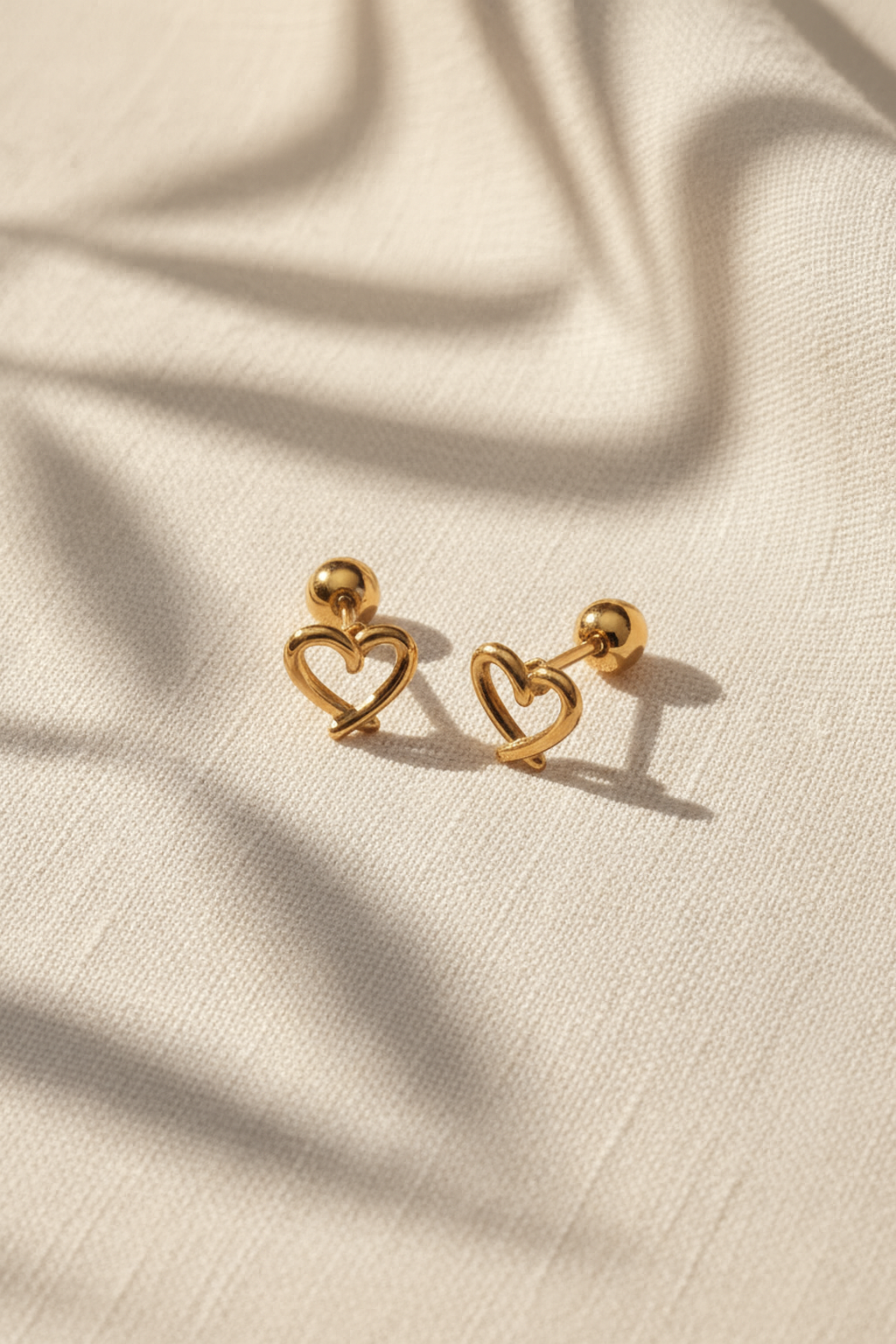 Gold heart-shaped earrings on a beige fabric background