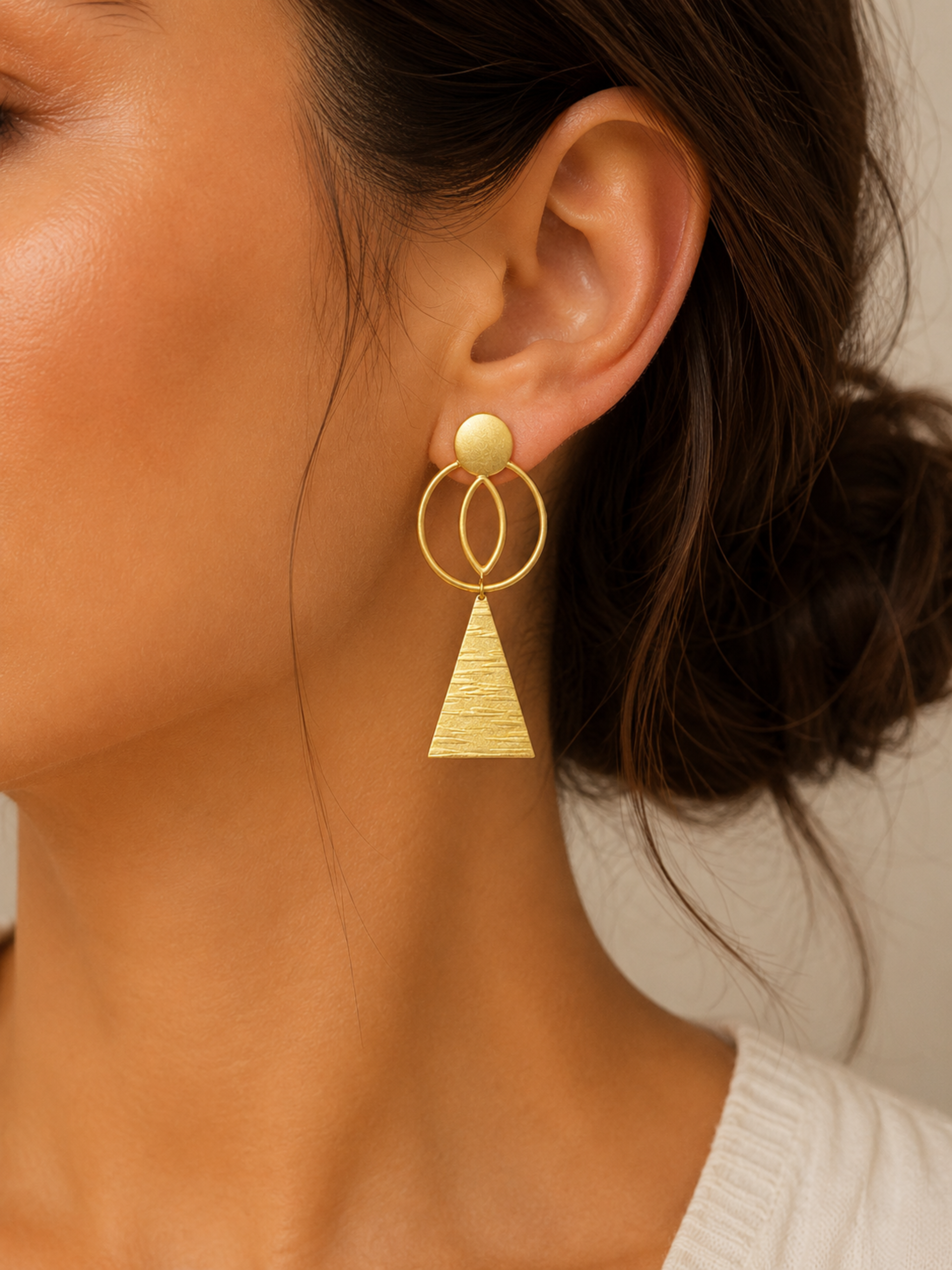 Gold earrings with geometric design worn by a person