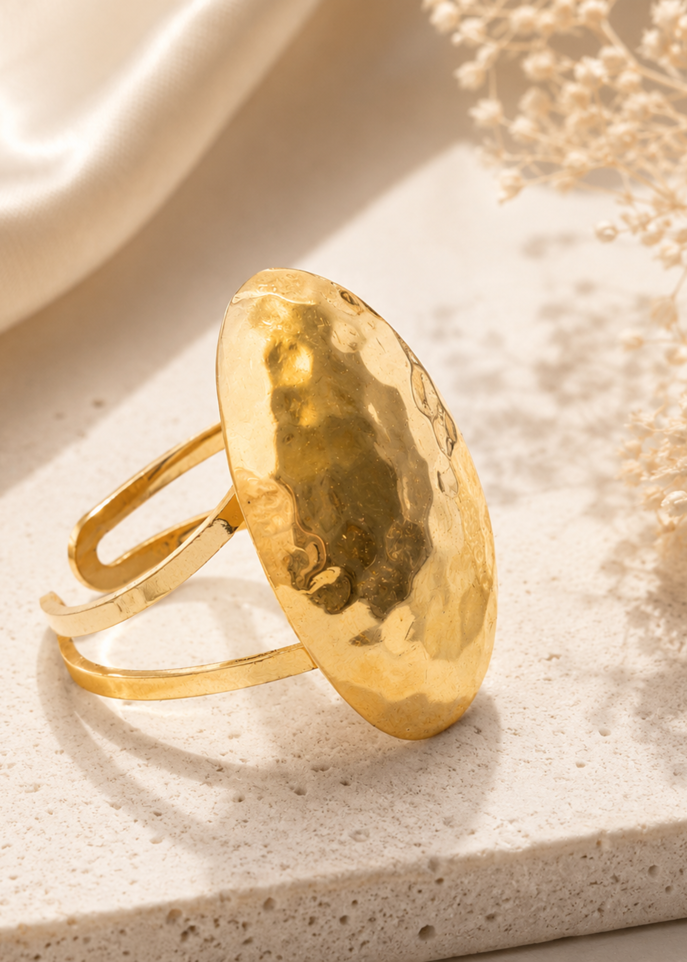 Gold ring with a textured design on a light stone surface with dried flowers.