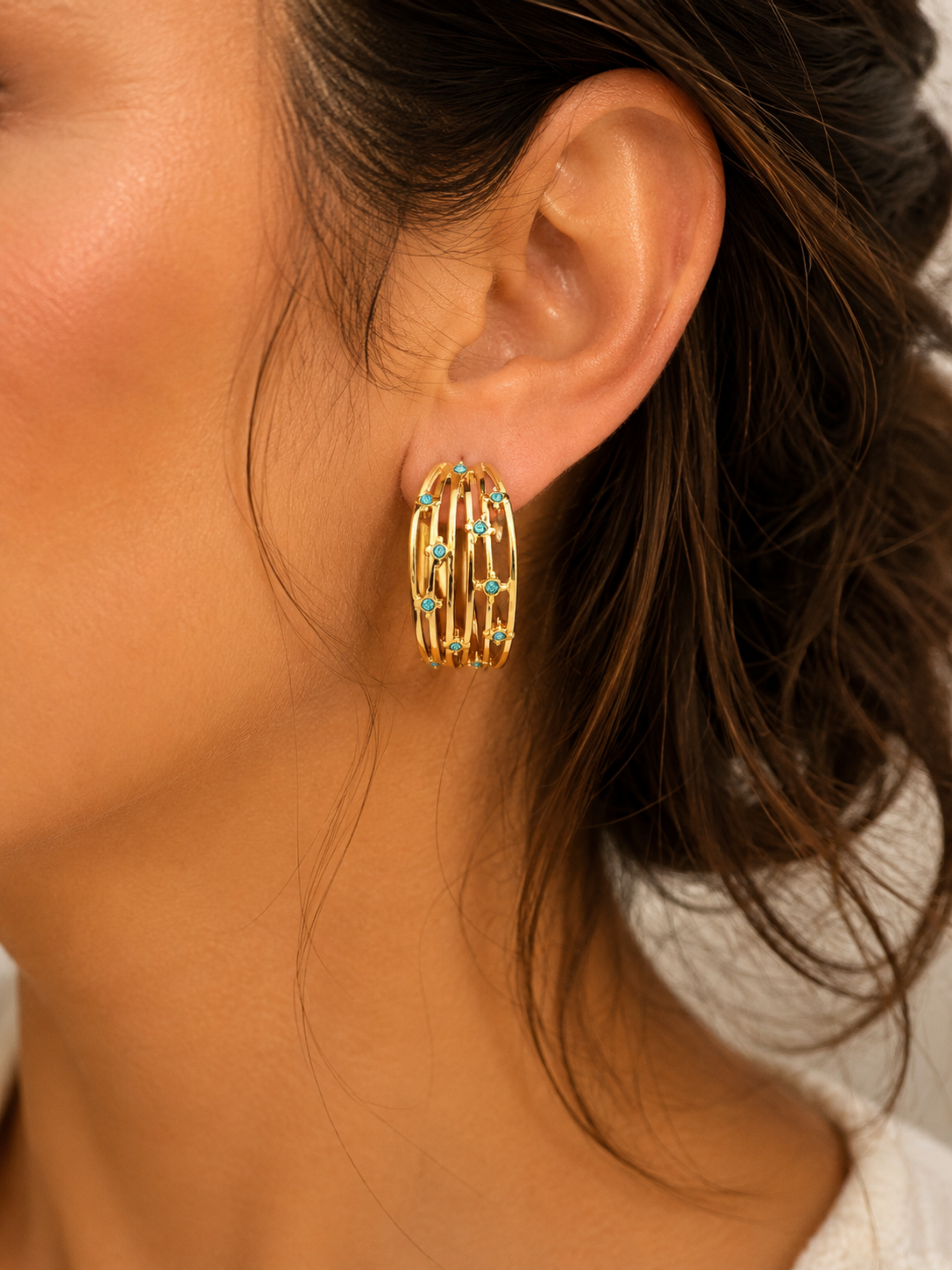 Close-up of a person wearing gold hoop earrings with green gemstones.