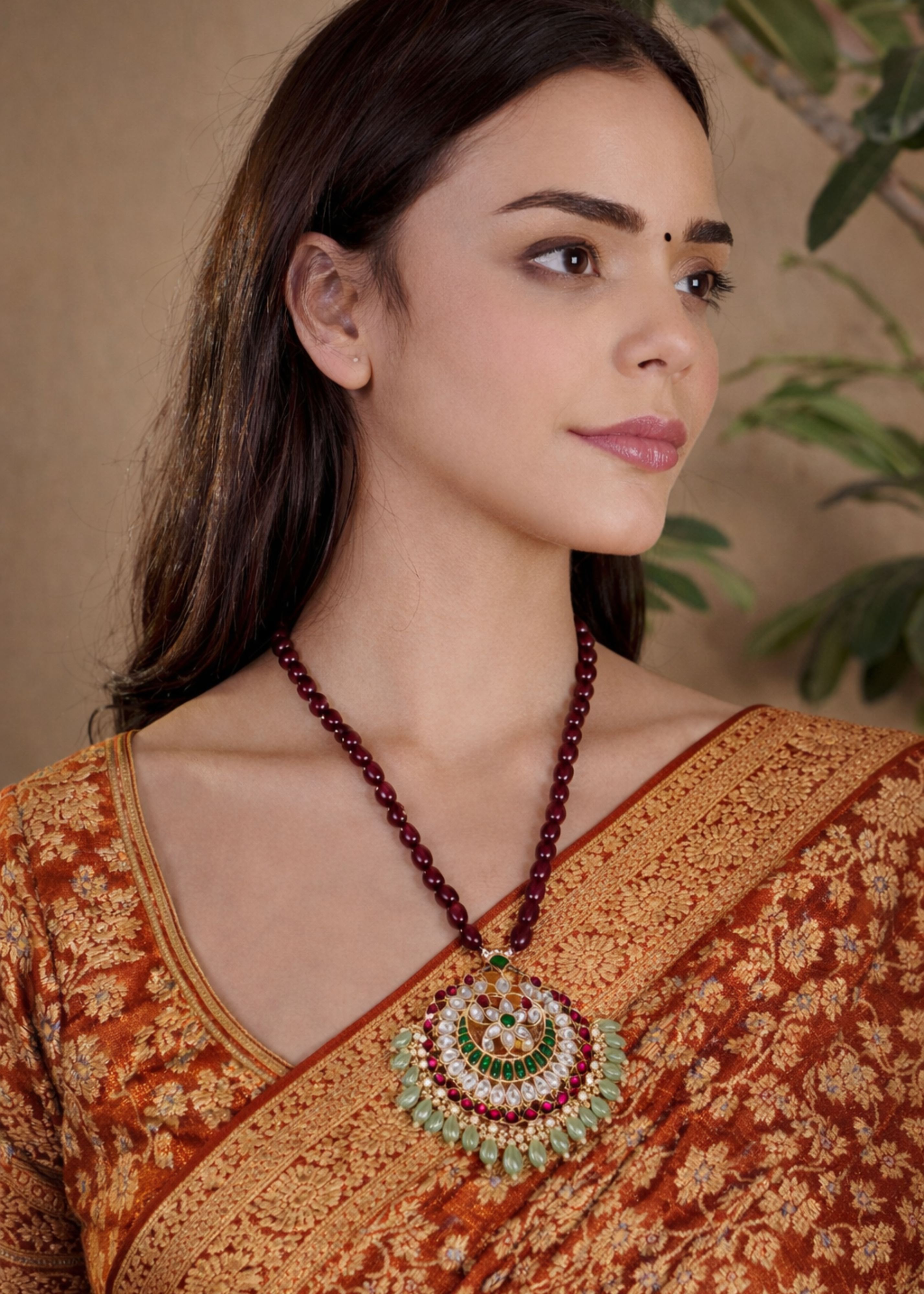Woman wearing a traditional saree with a prominent necklace, set against a neutral background.