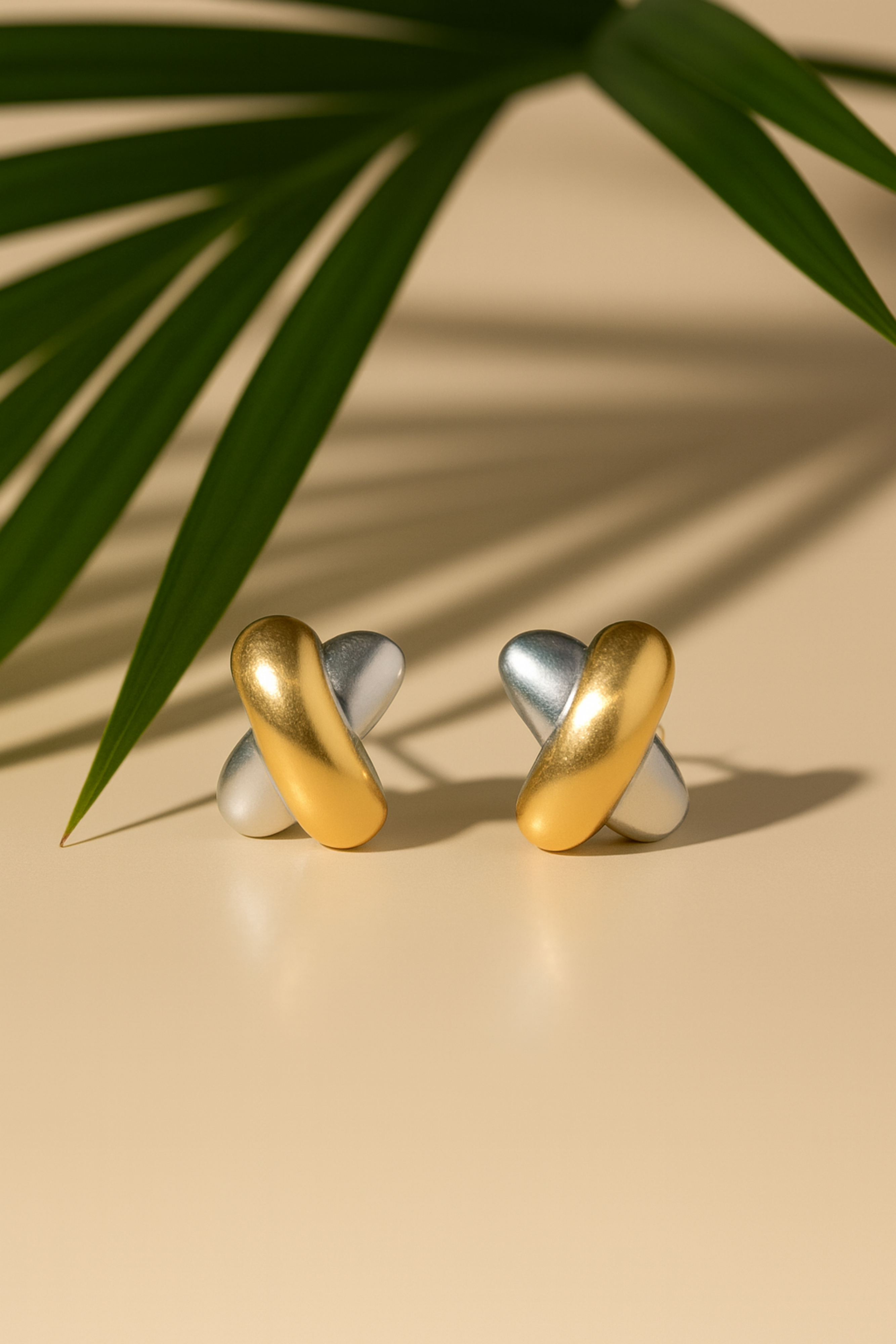 Gold and silver earrings on a beige surface with a leaf in the background