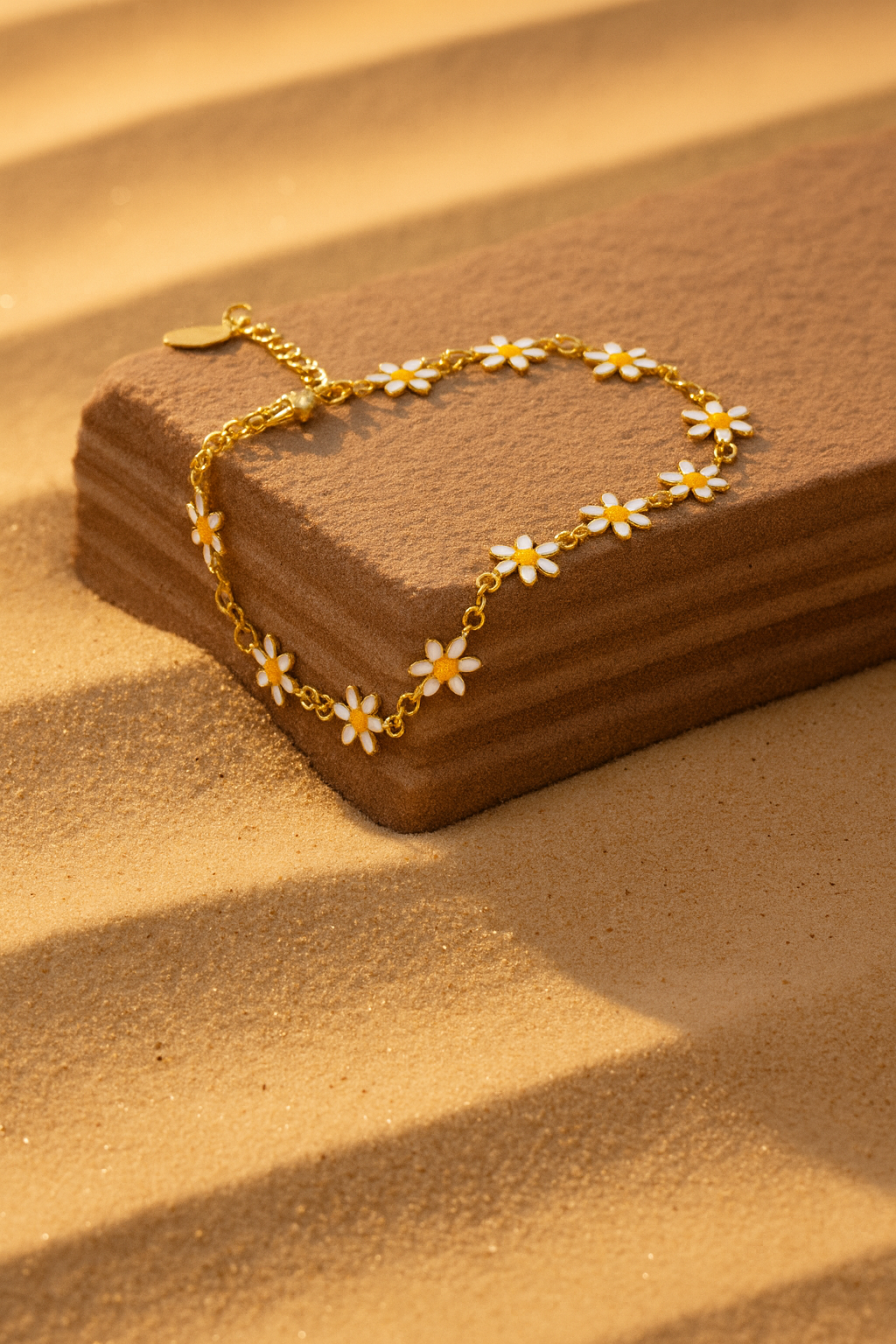 Gold bracelet with white flowers on a brown wooden block against a sandy background