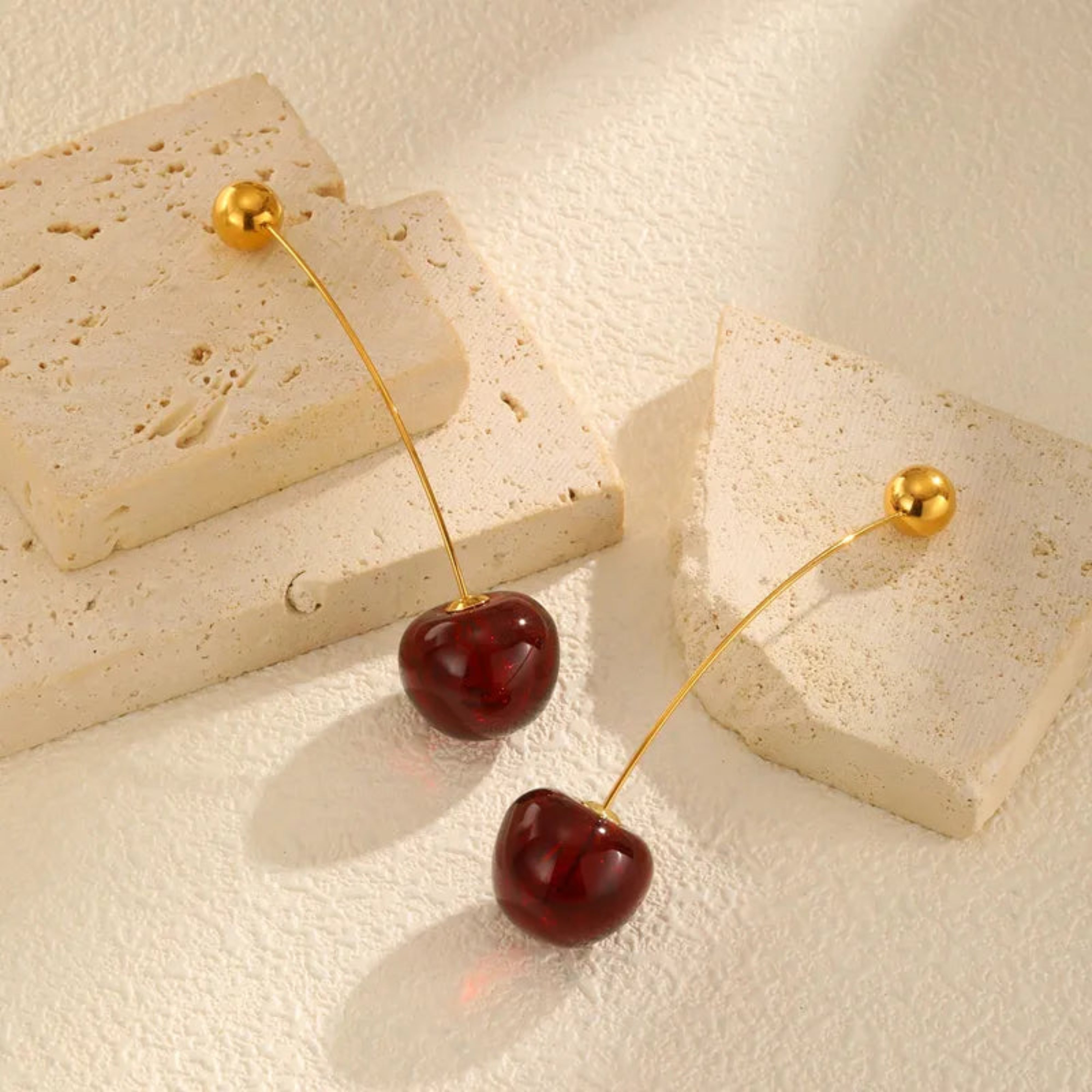 Cherry-shaped earrings on a textured beige surface