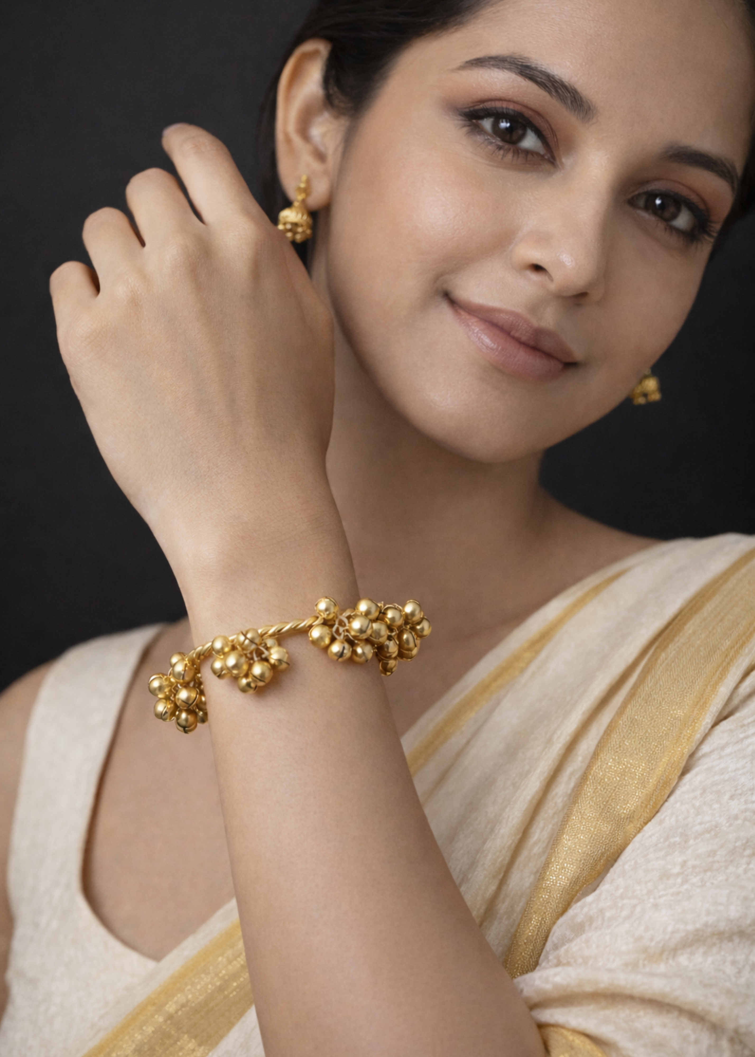 Woman wearing gold jewelry including earrings and a bracelet, with a plain background