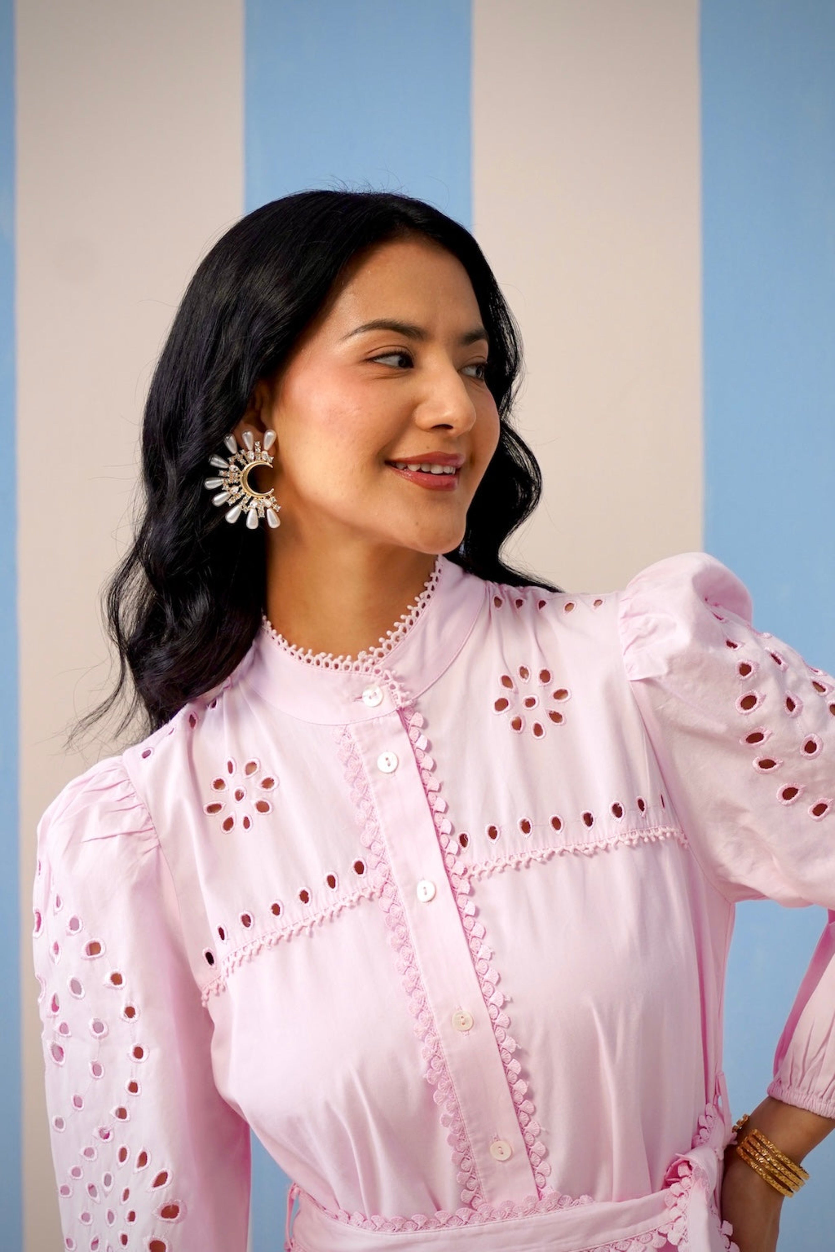 Woman wearing a pink blouse with intricate designs against a striped background