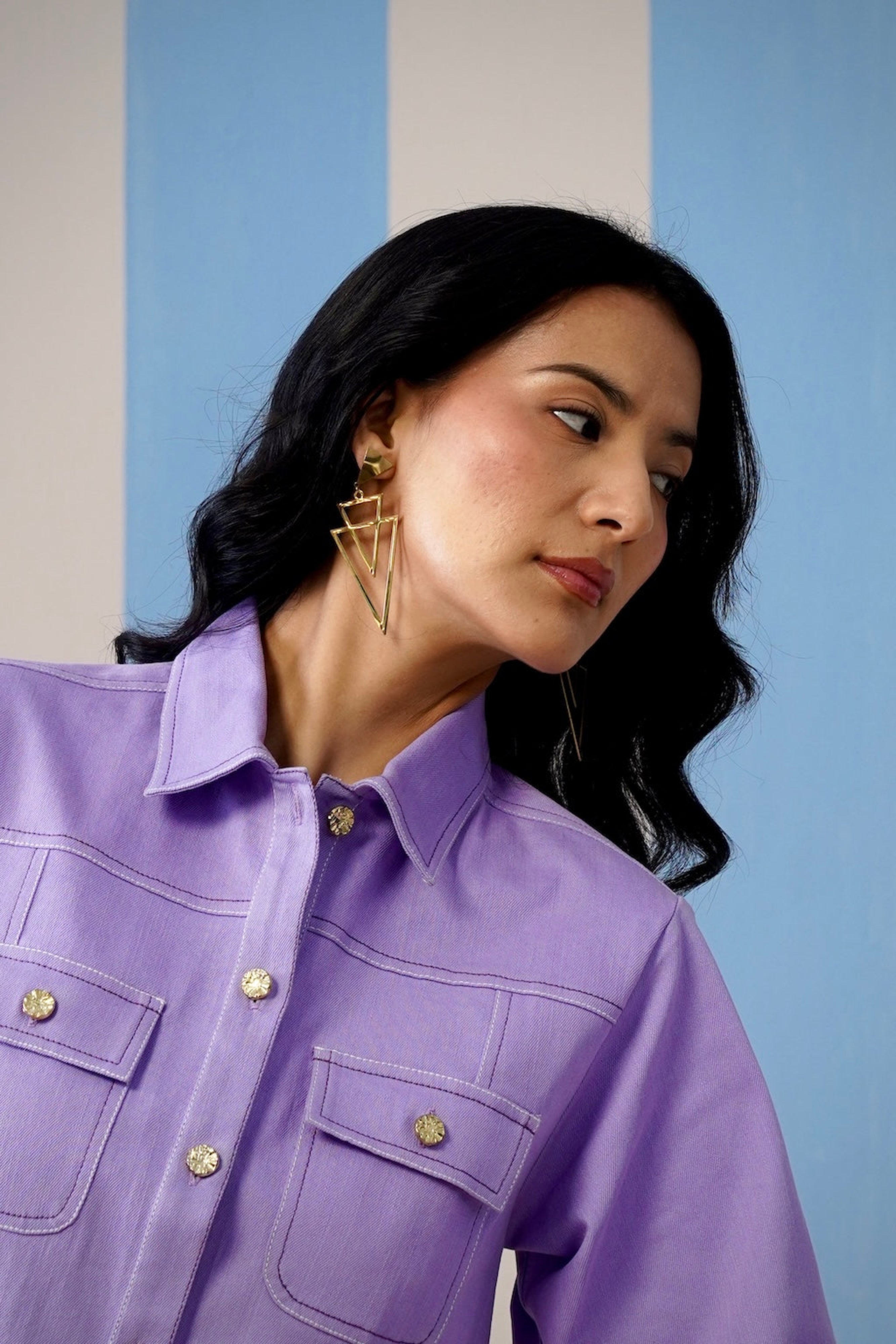Woman wearing a purple shirt with gold buttons against a light blue wall.