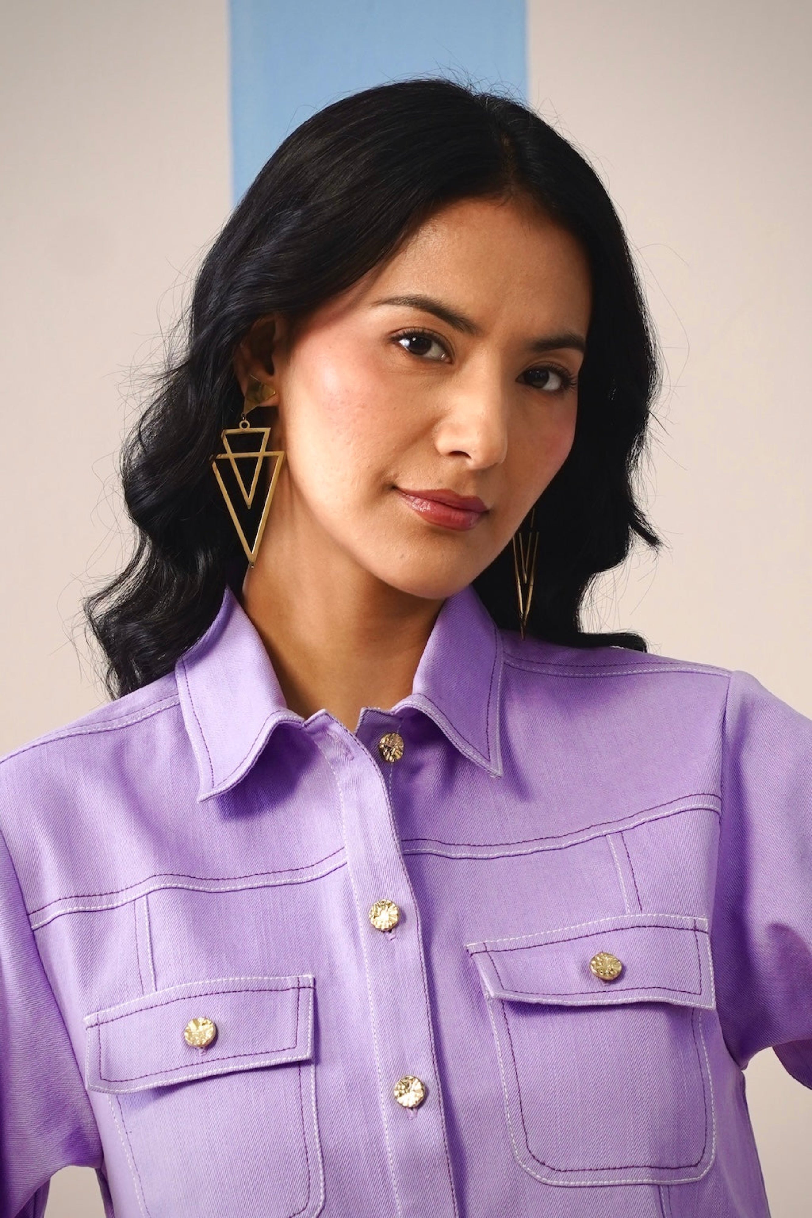 Woman wearing a purple shirt with gold buttons against a plain background