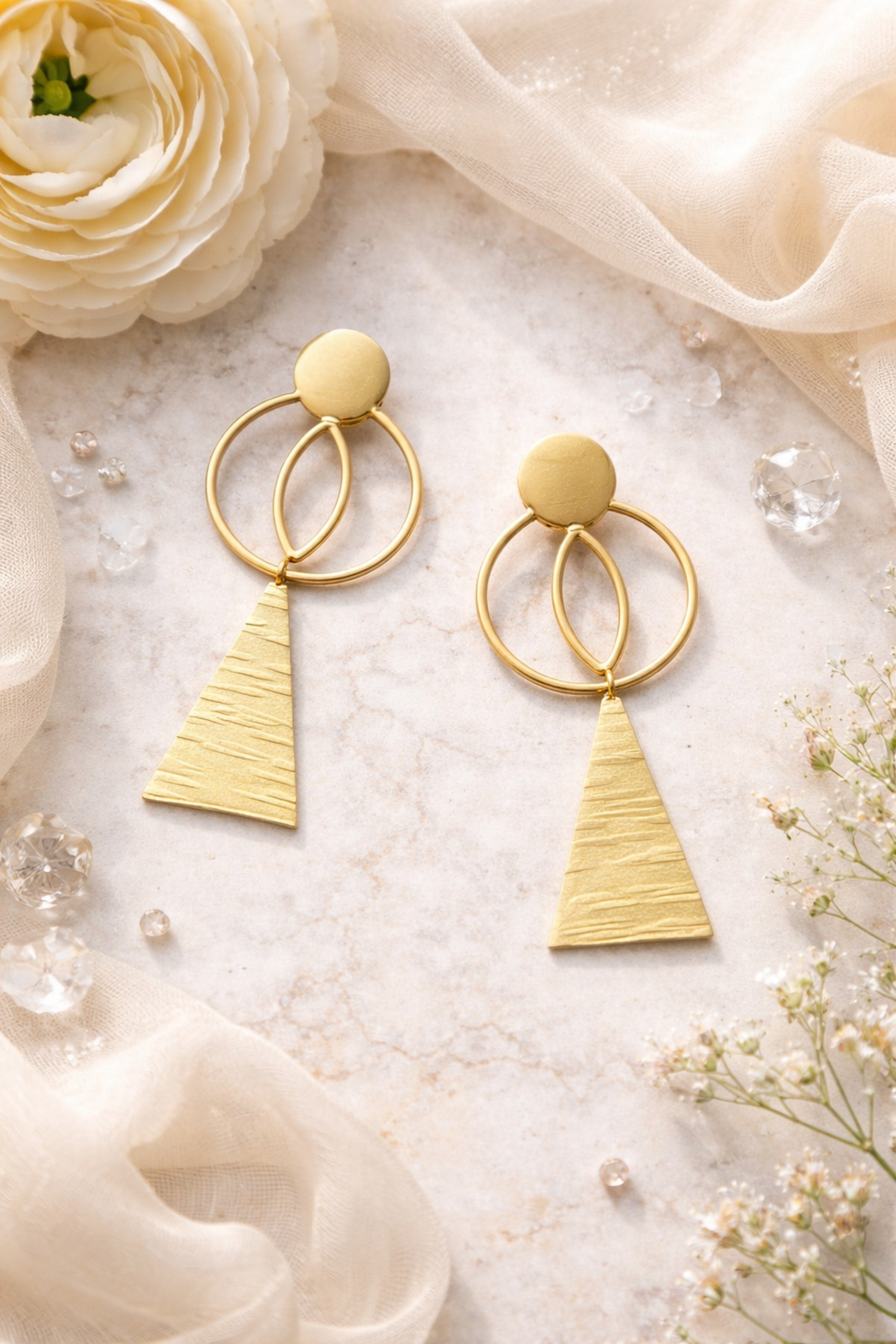 Gold earrings with geometric design on a soft white background with flowers