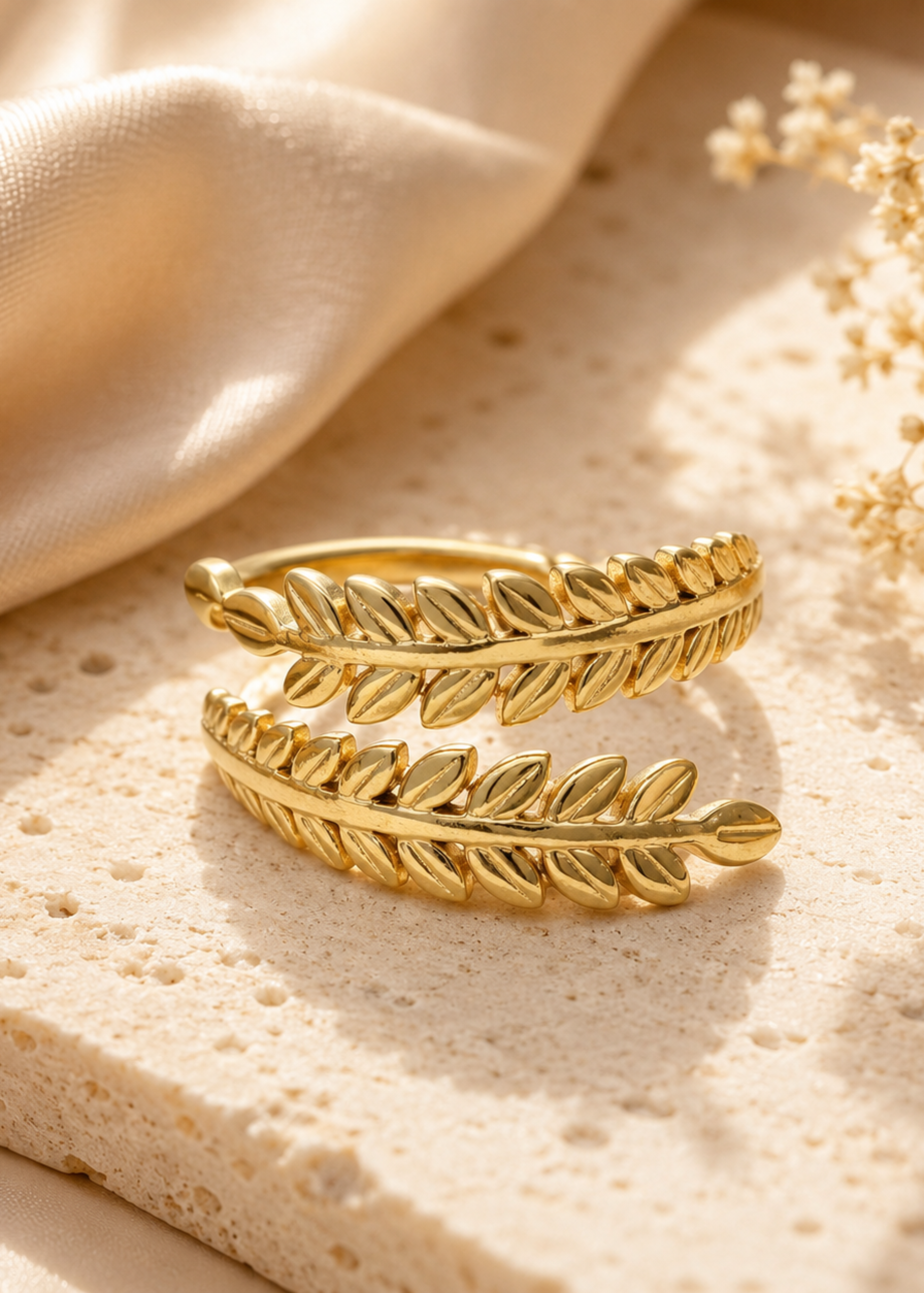 Gold leaf-shaped ring on a textured beige surface with a soft focus background