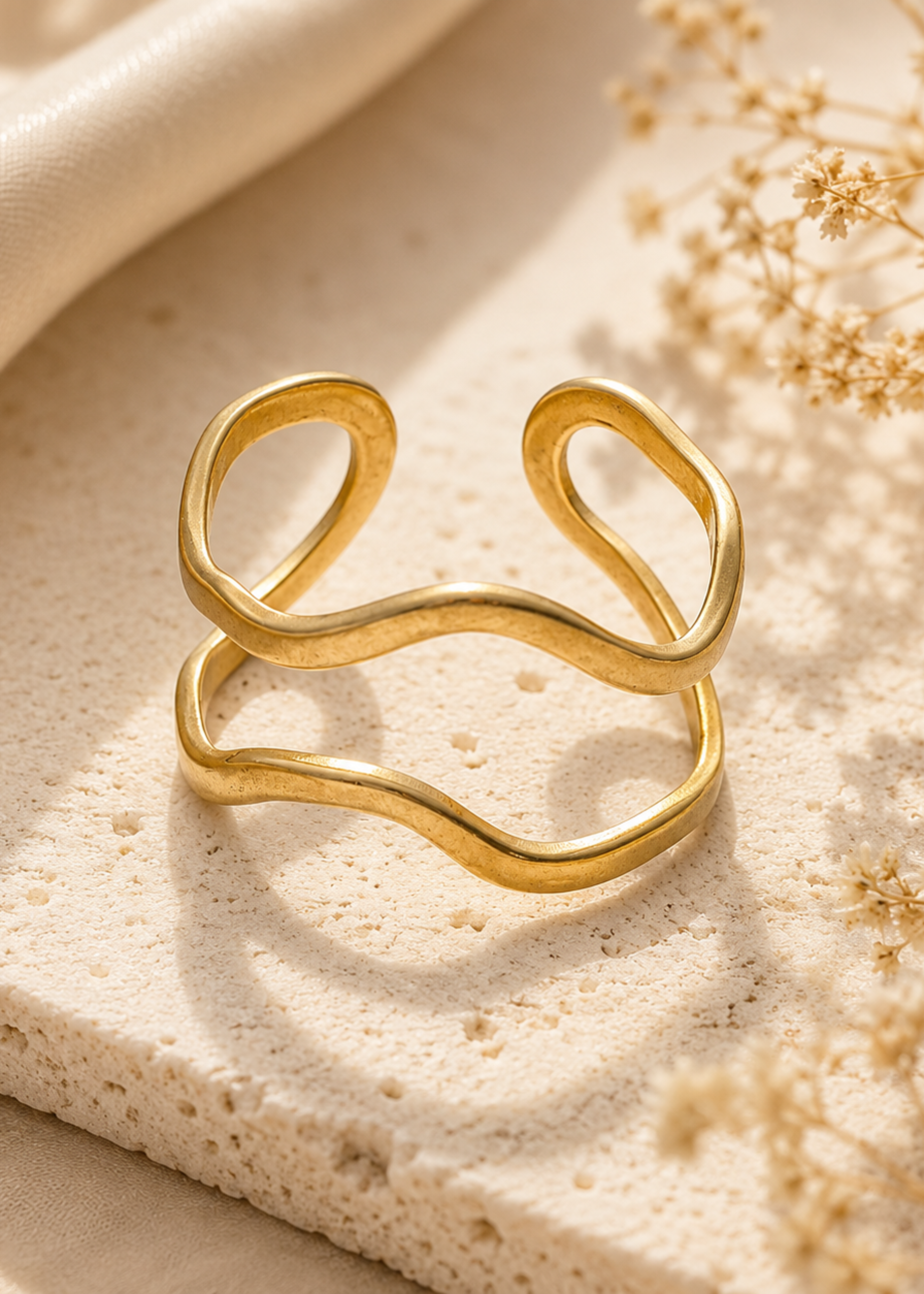 Gold ring on a textured beige surface with dried flowers