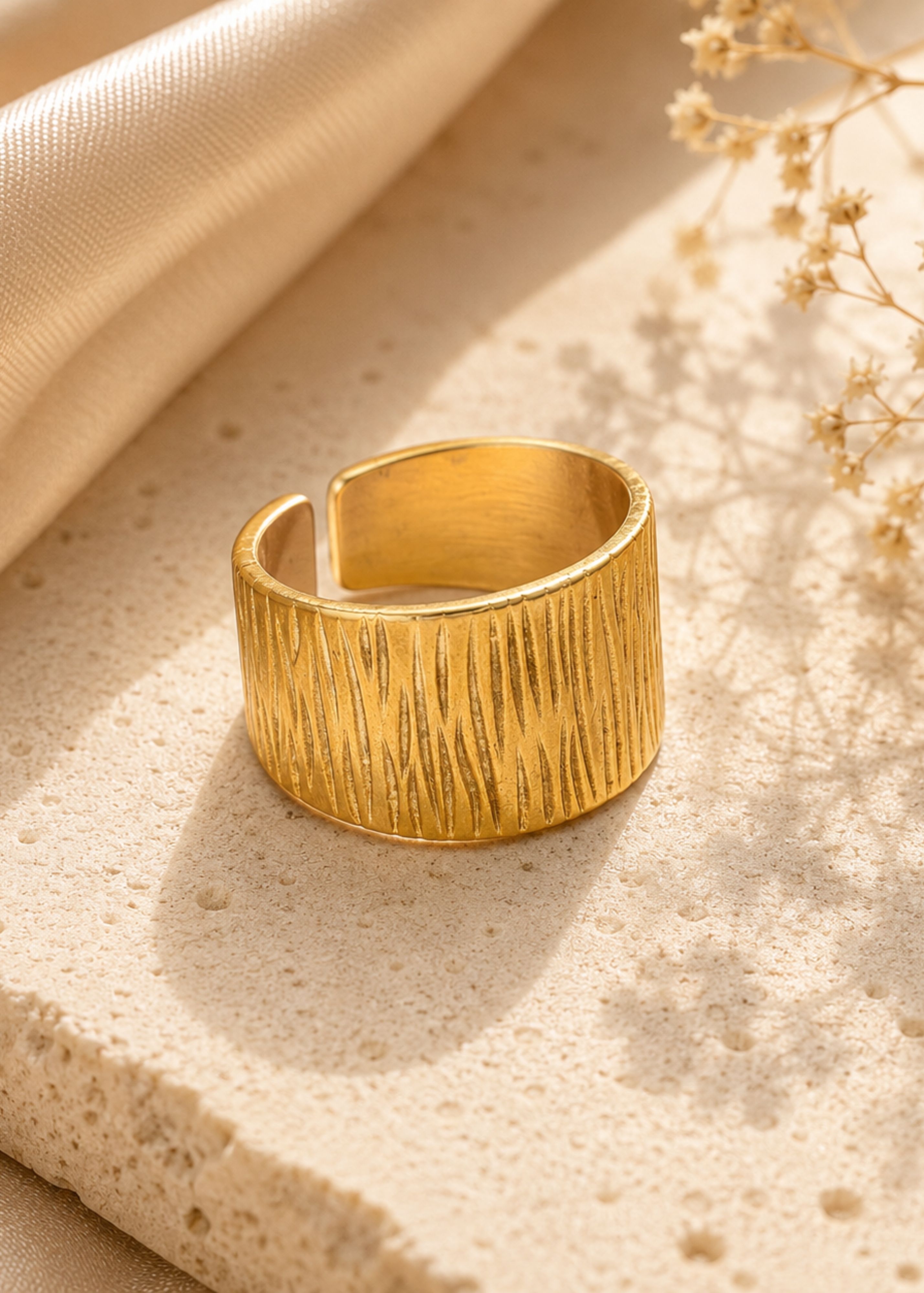 Gold ring on a textured beige surface with fabric and dried flowers
