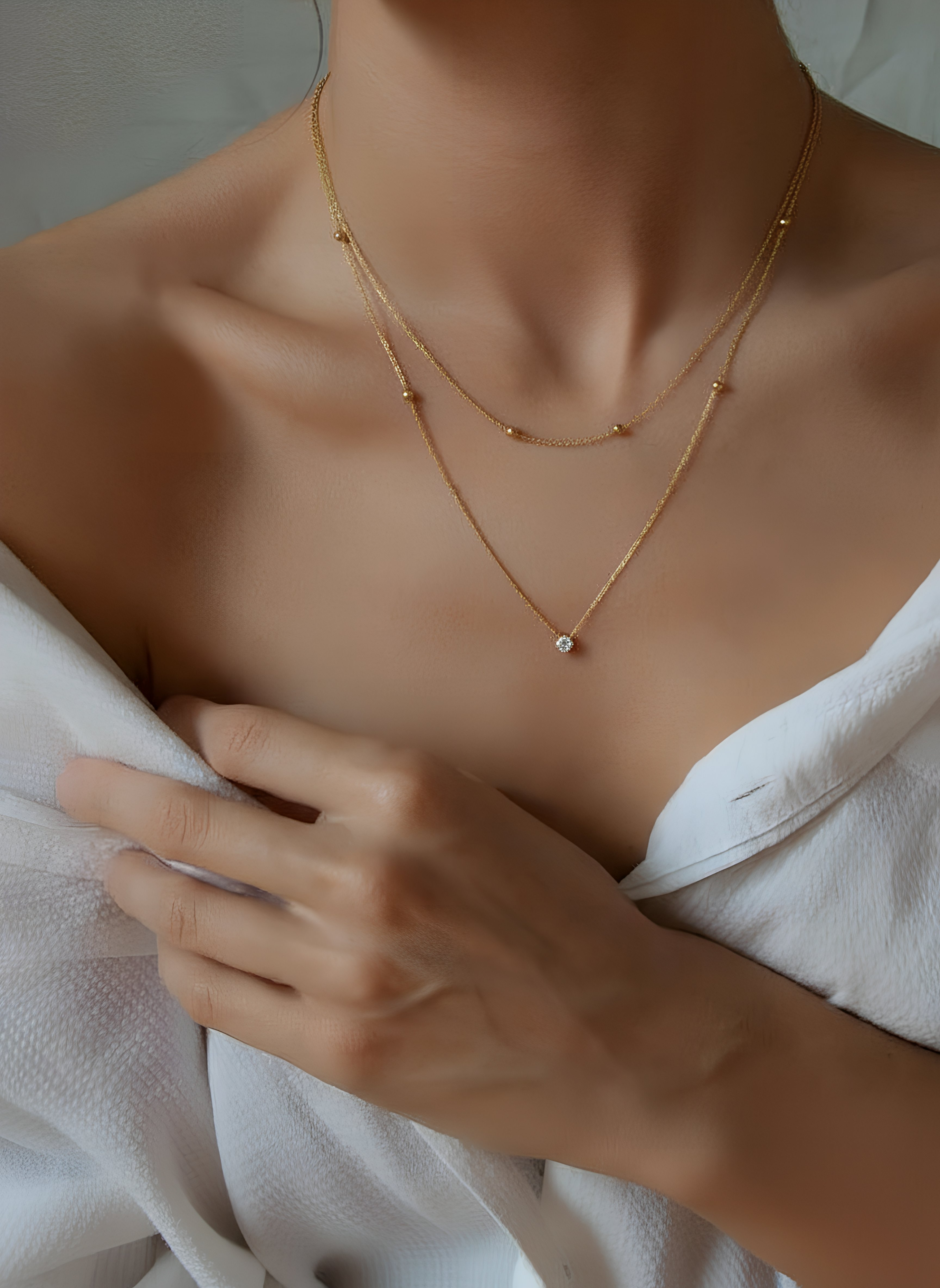 Close-up of a person wearing a gold necklace with a soft white background