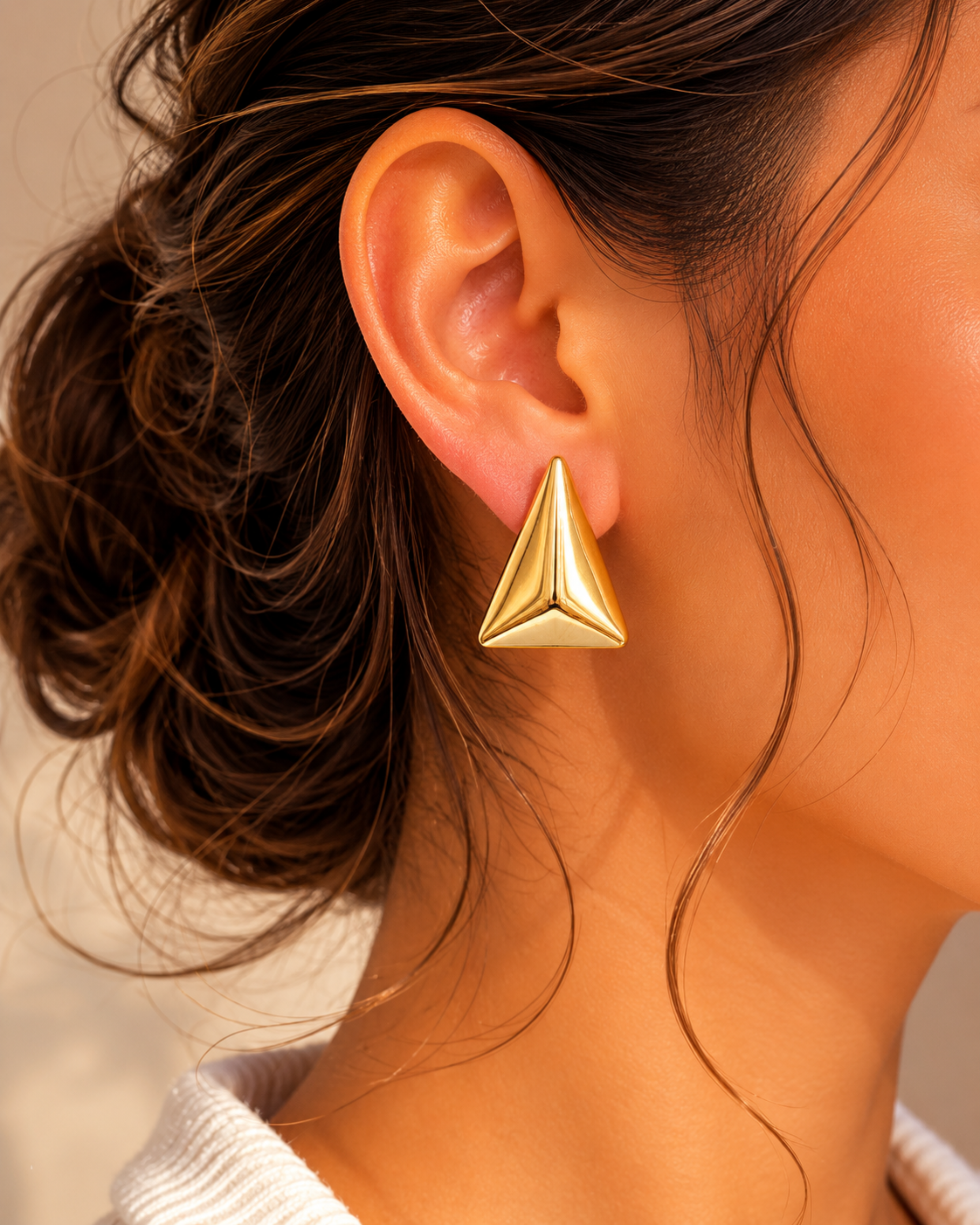 Gold pyramid-shaped earring worn by a person with a neutral background