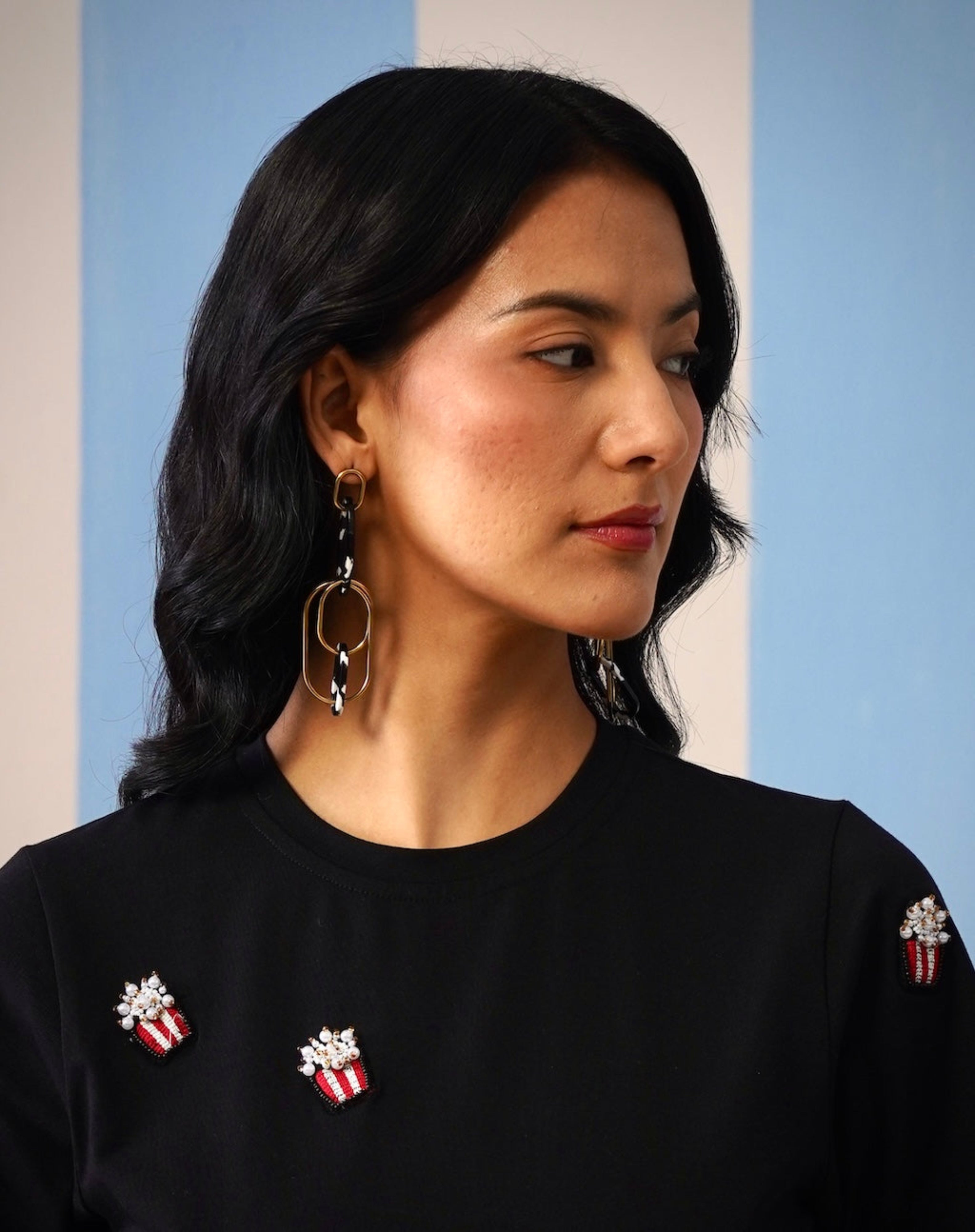 Woman wearing a black top with decorative pins, focusing on her earrings.