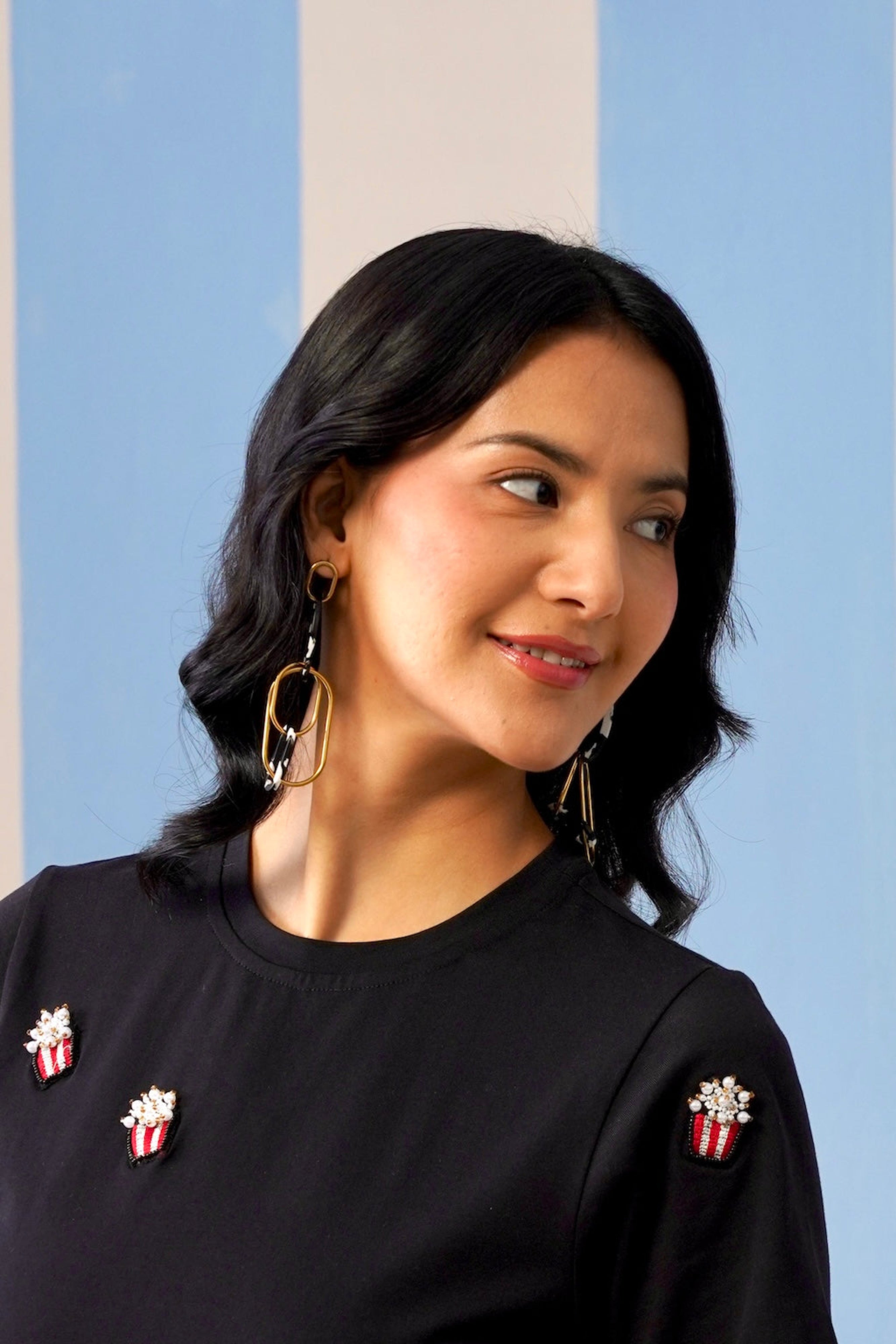 Woman wearing a black top with decorative pins against a striped background