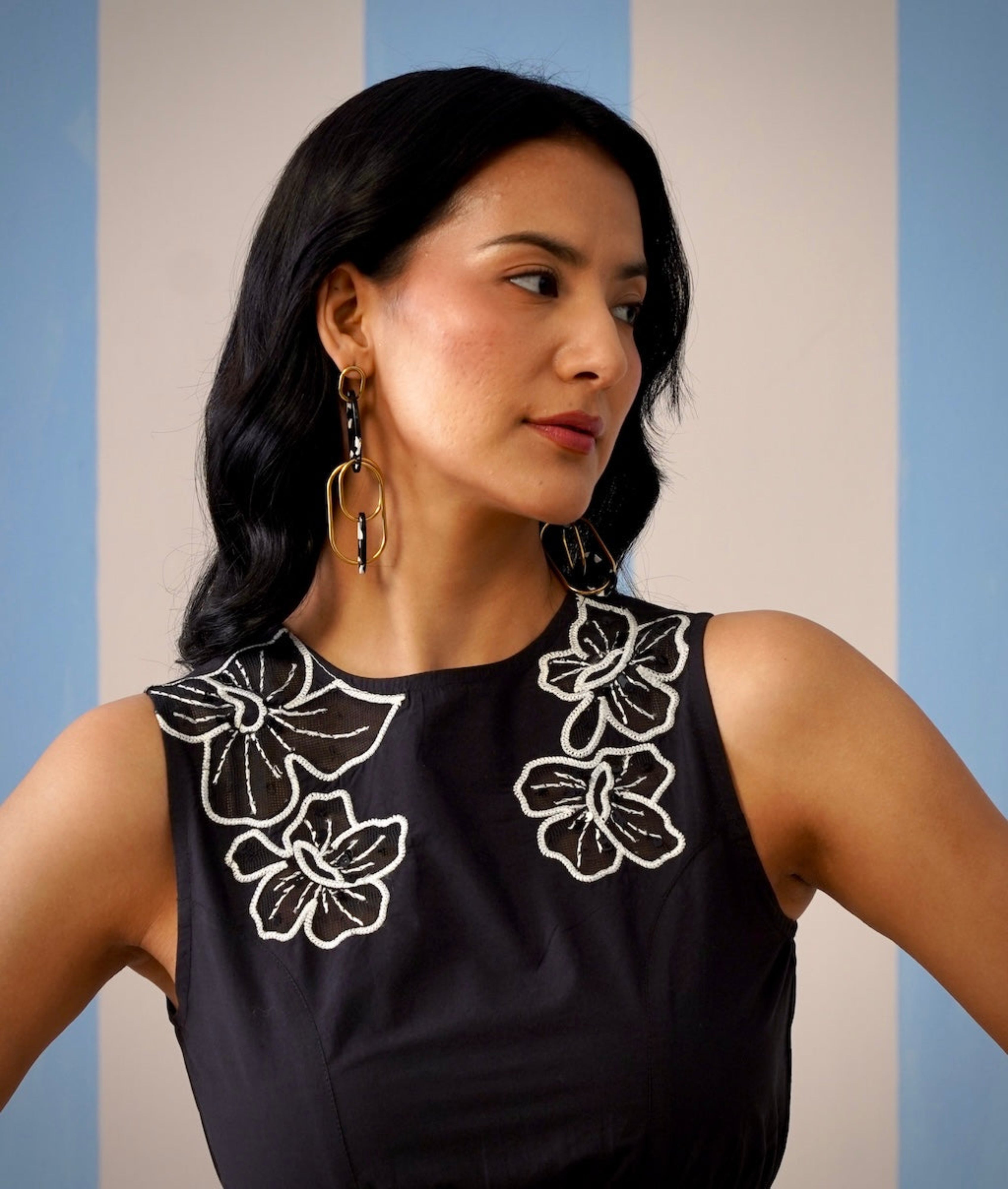 Woman wearing a black sleeveless top with white floral patterns against a striped background