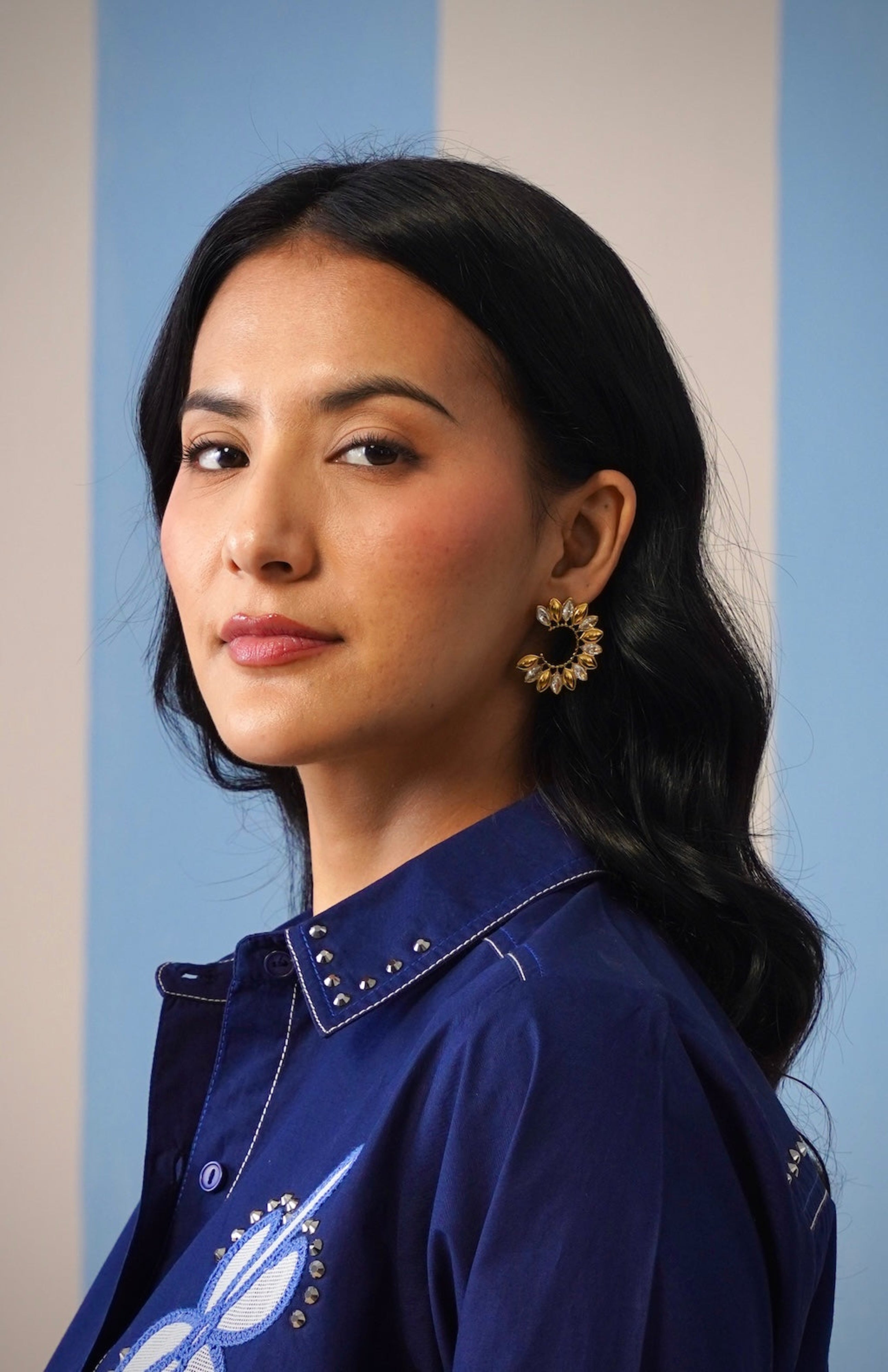 Woman wearing a blue shirt with decorative elements against a light blue wall.