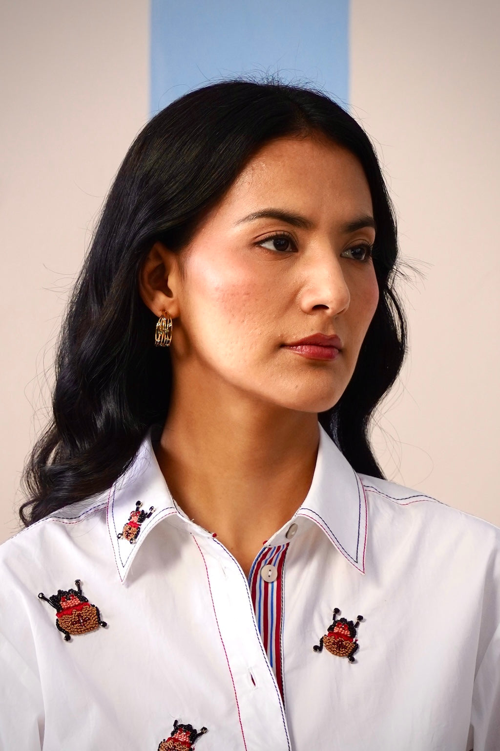 Woman wearing a white shirt with embroidered designs against a plain background