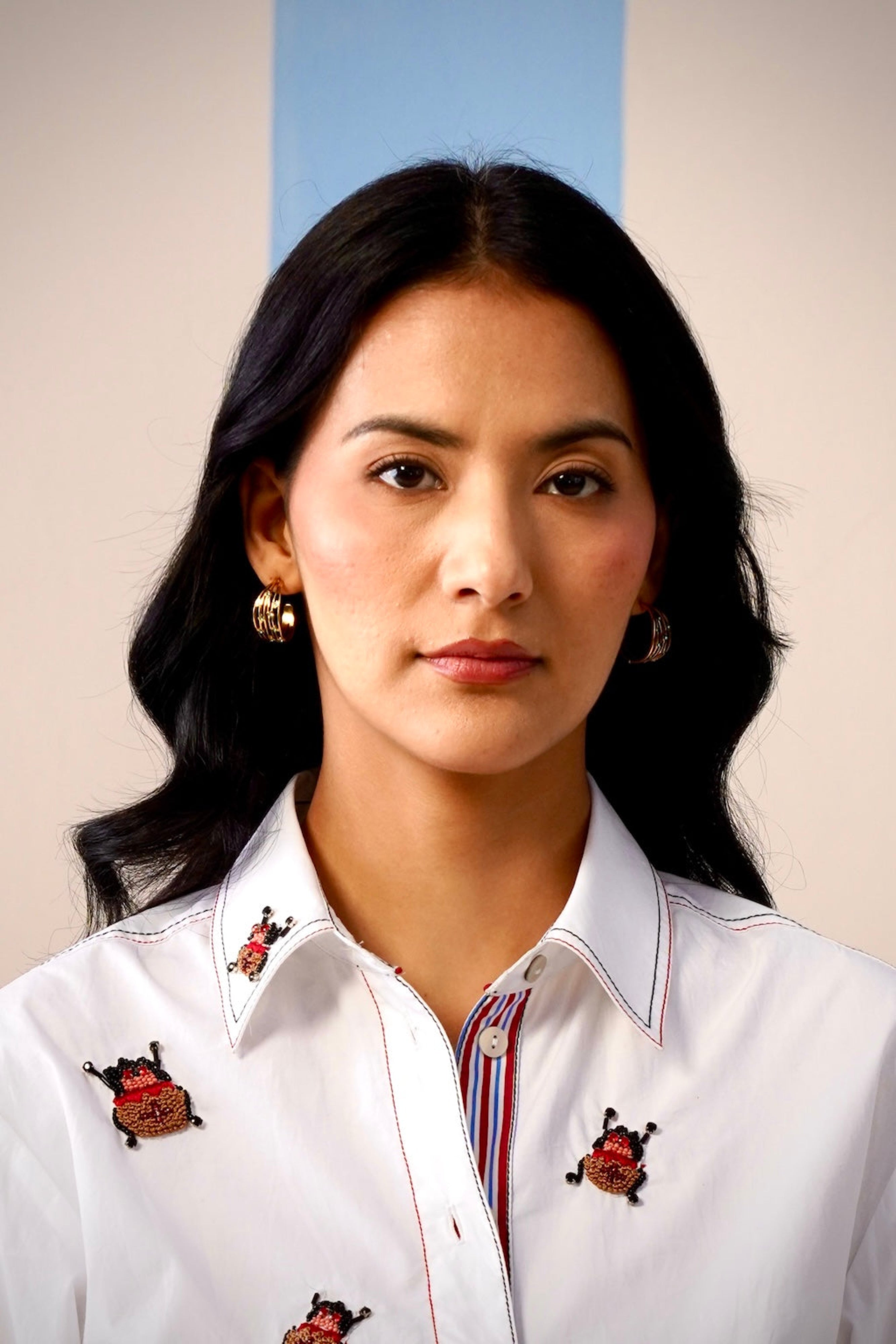 Woman wearing a white shirt with embroidered designs on a plain background