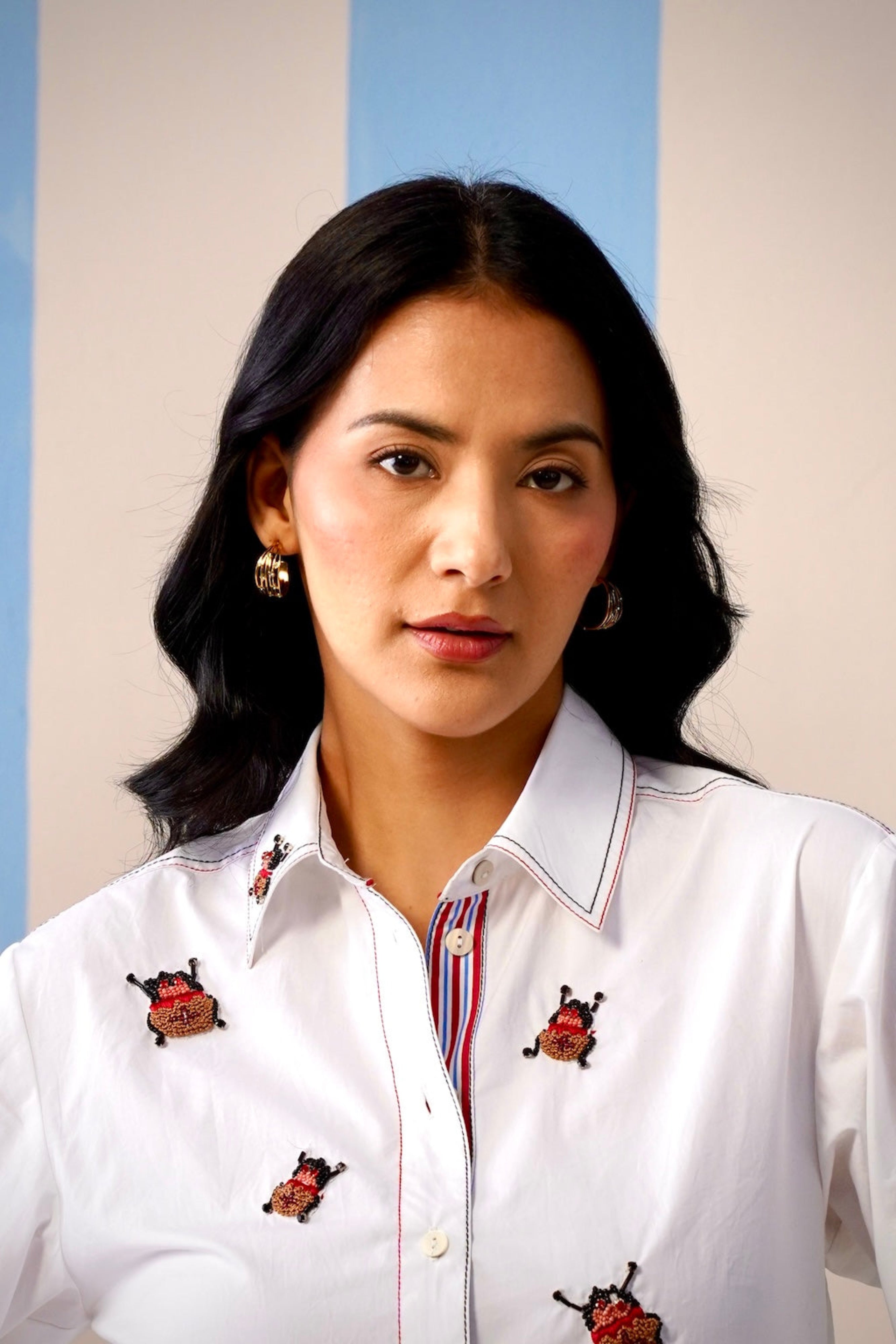 Woman wearing a white shirt with embroidered designs against a blue and beige background