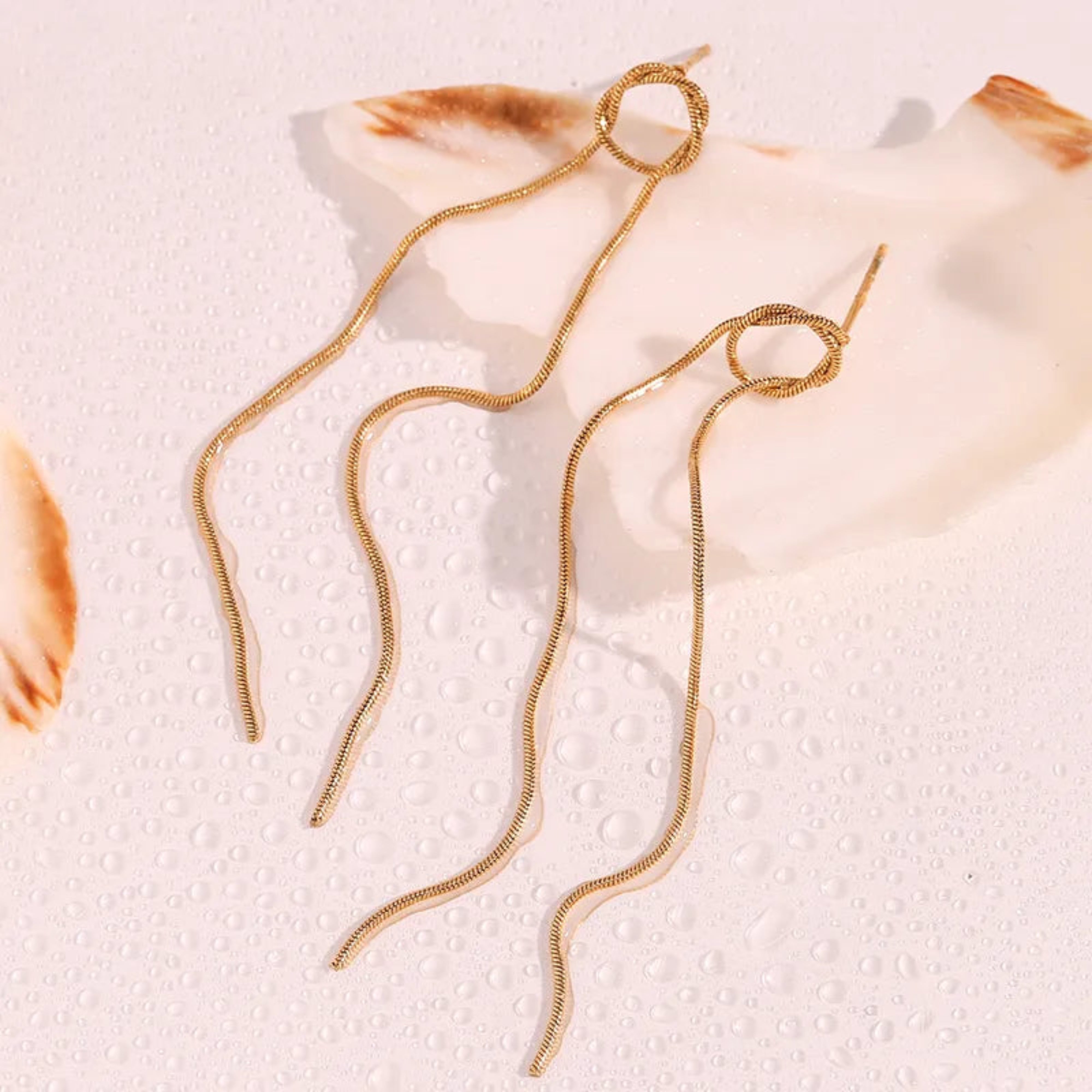 Gold chain necklace on a textured beige surface with seashells.