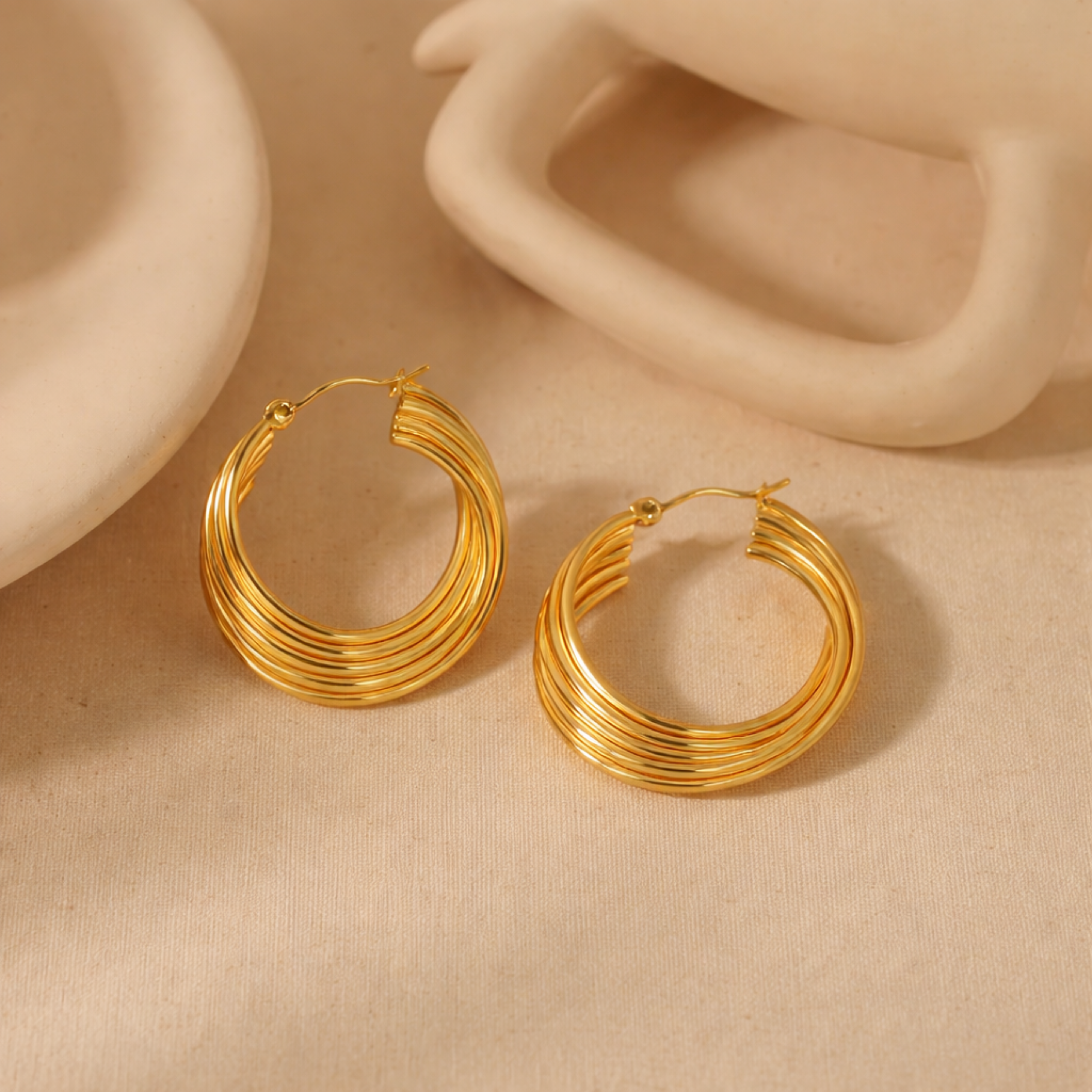 Gold hoop earrings on a beige surface with a neutral background