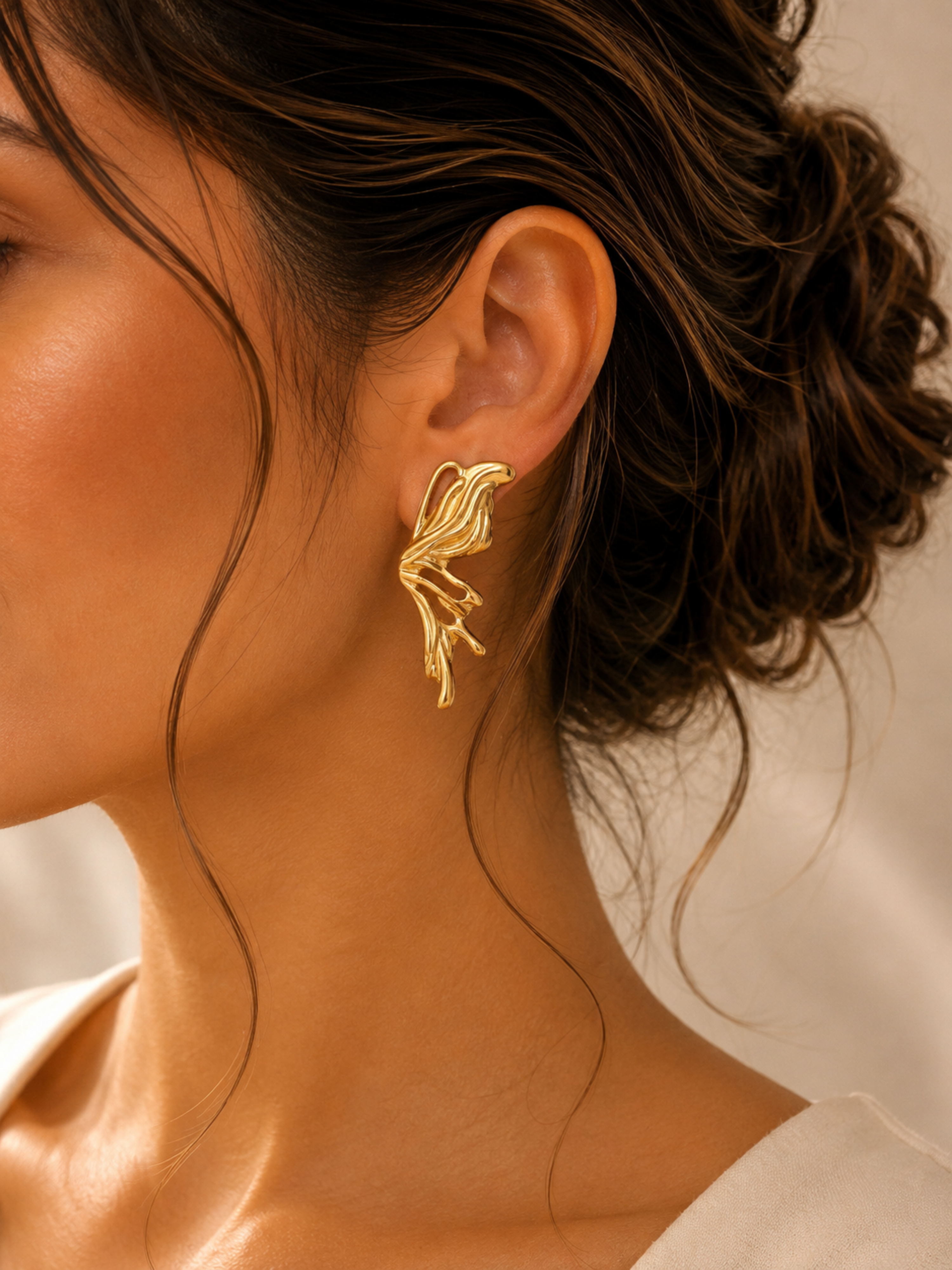 Close-up of a person wearing gold earrings with a neutral background
