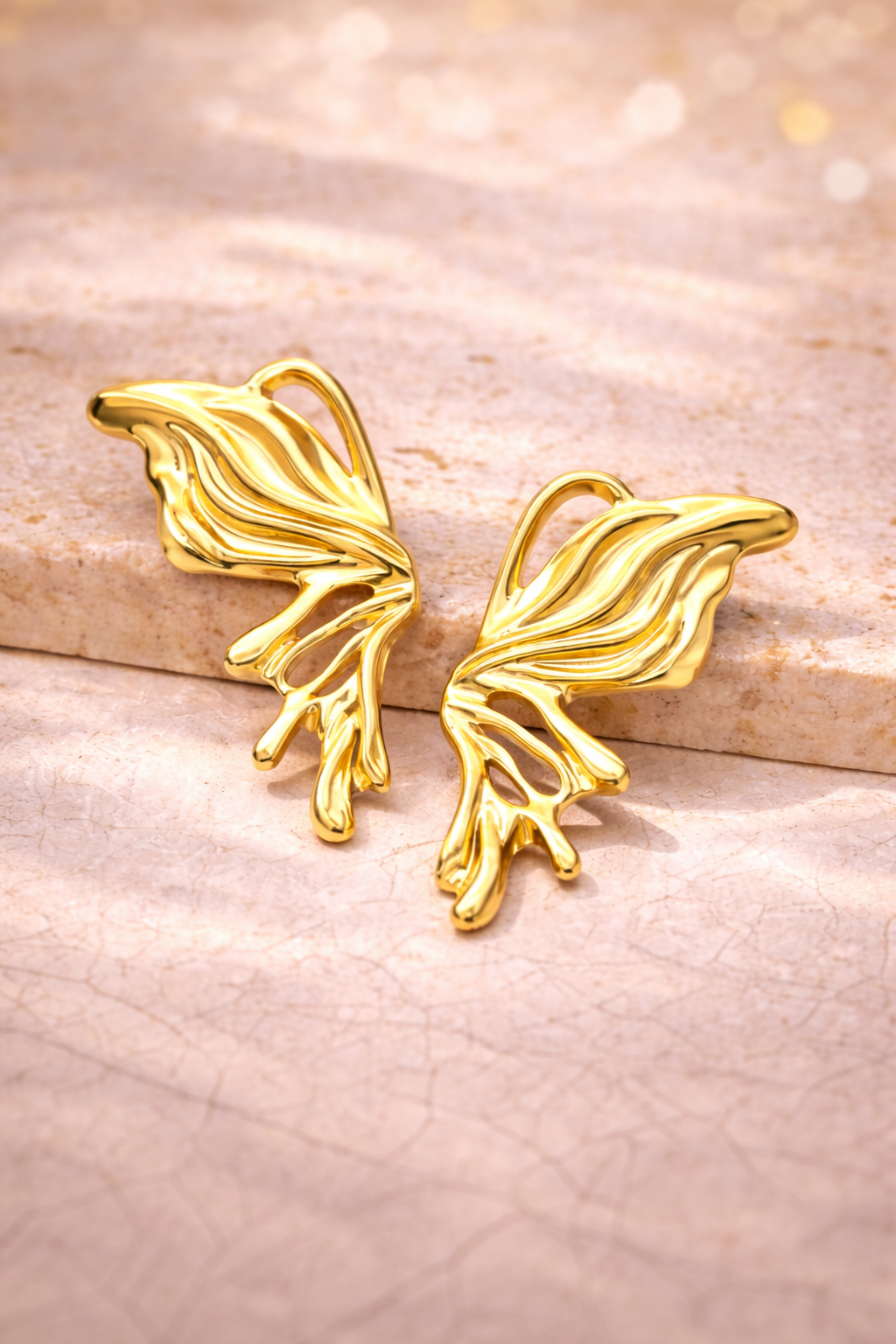 Gold leaf-shaped earrings on a textured beige surface