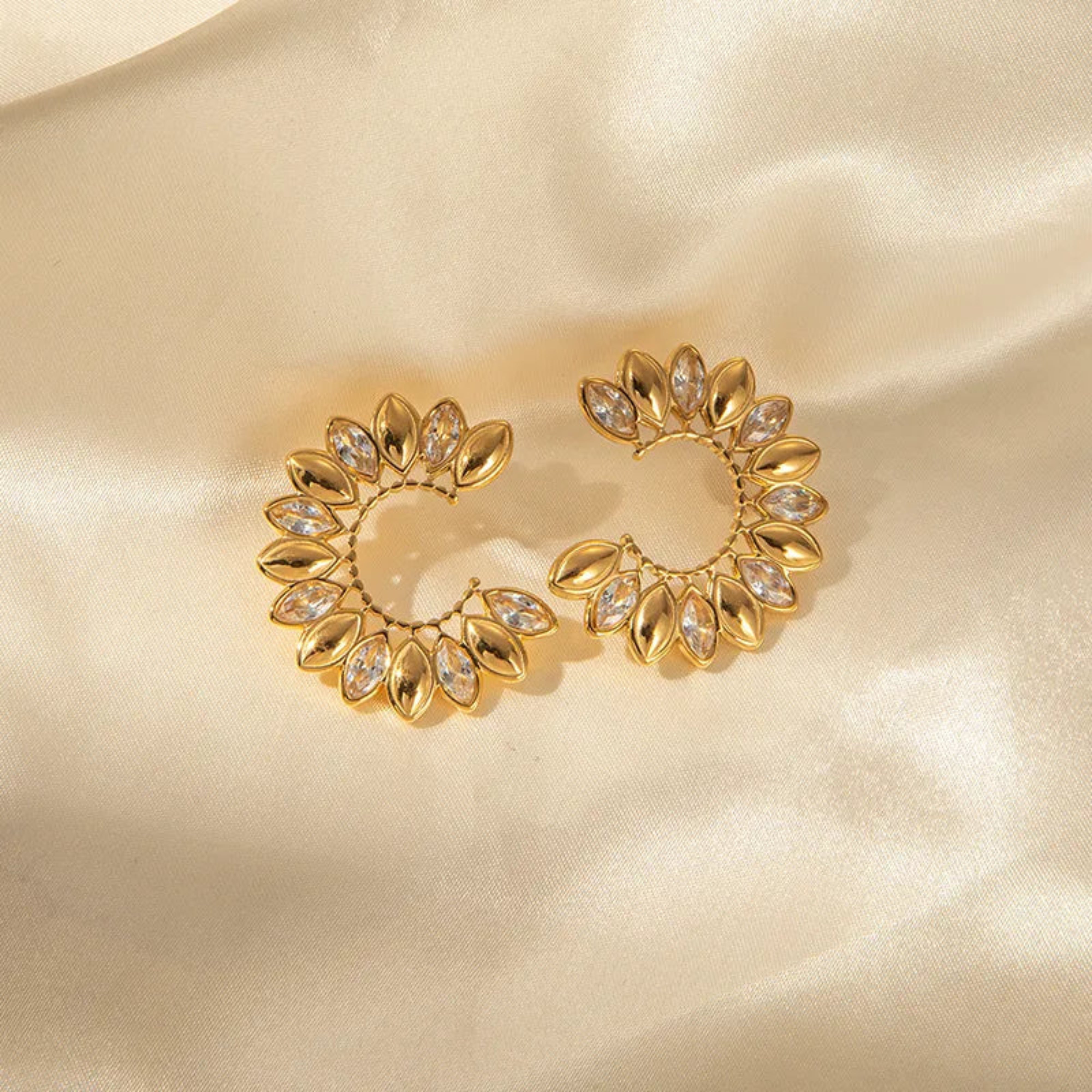 Gold earrings with gemstones on a beige satin background