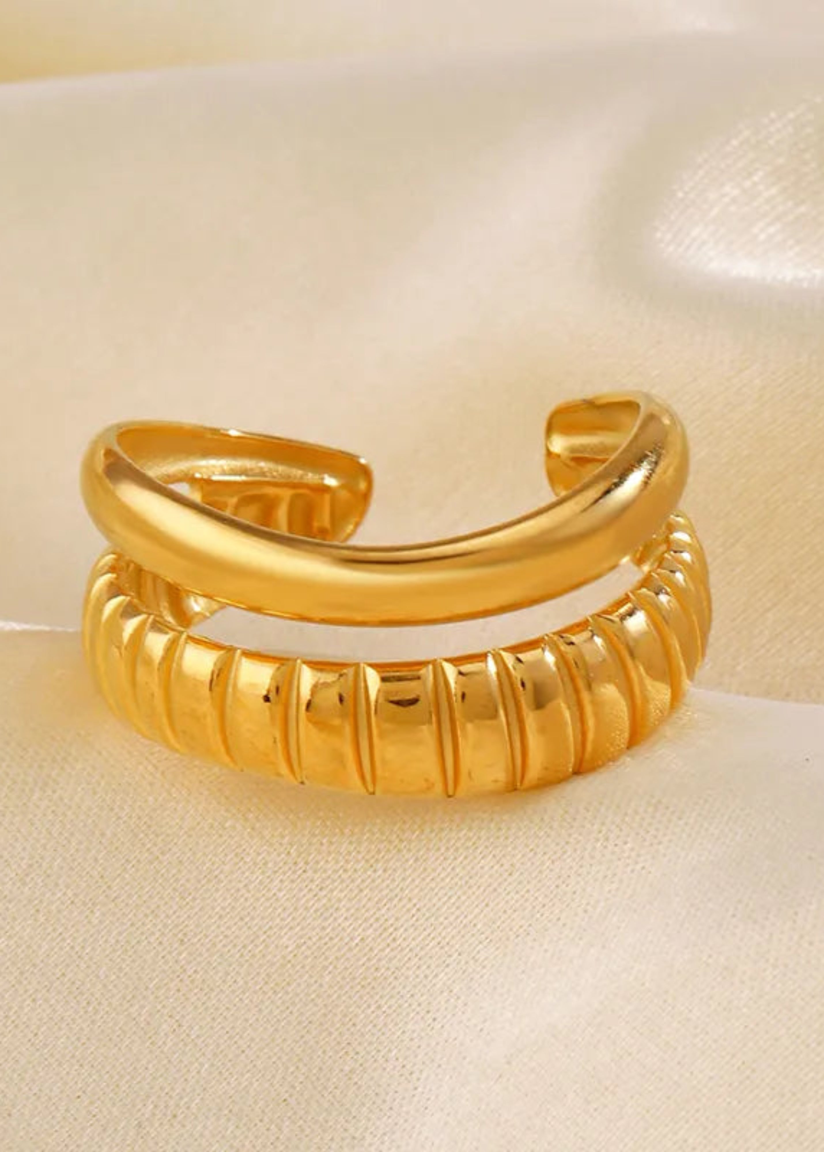 Gold ring with ribbed design on a beige fabric background